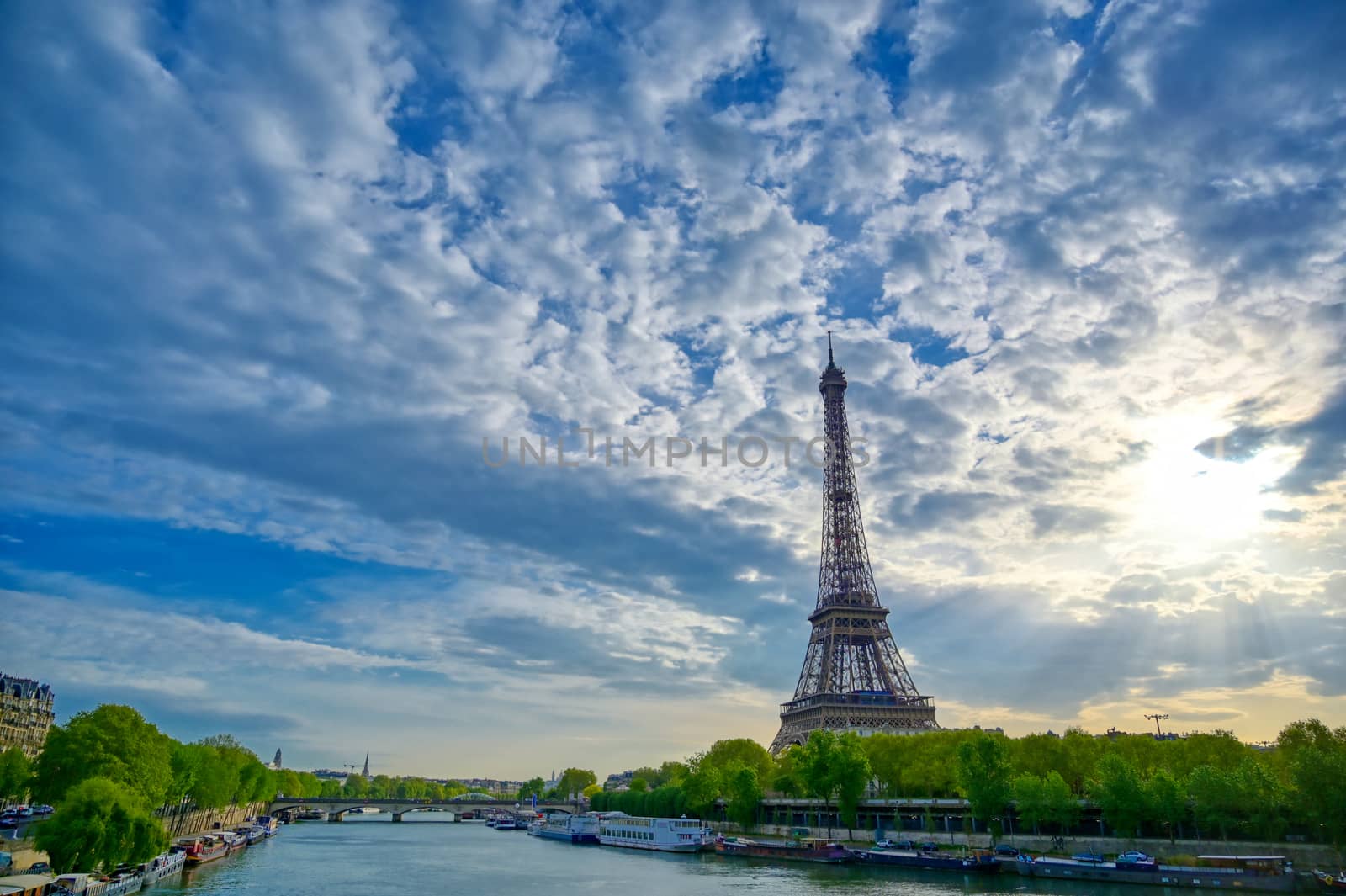 The Eiffel Tower across the Seine River in Paris, France on a sunny day with beautiful clouds.