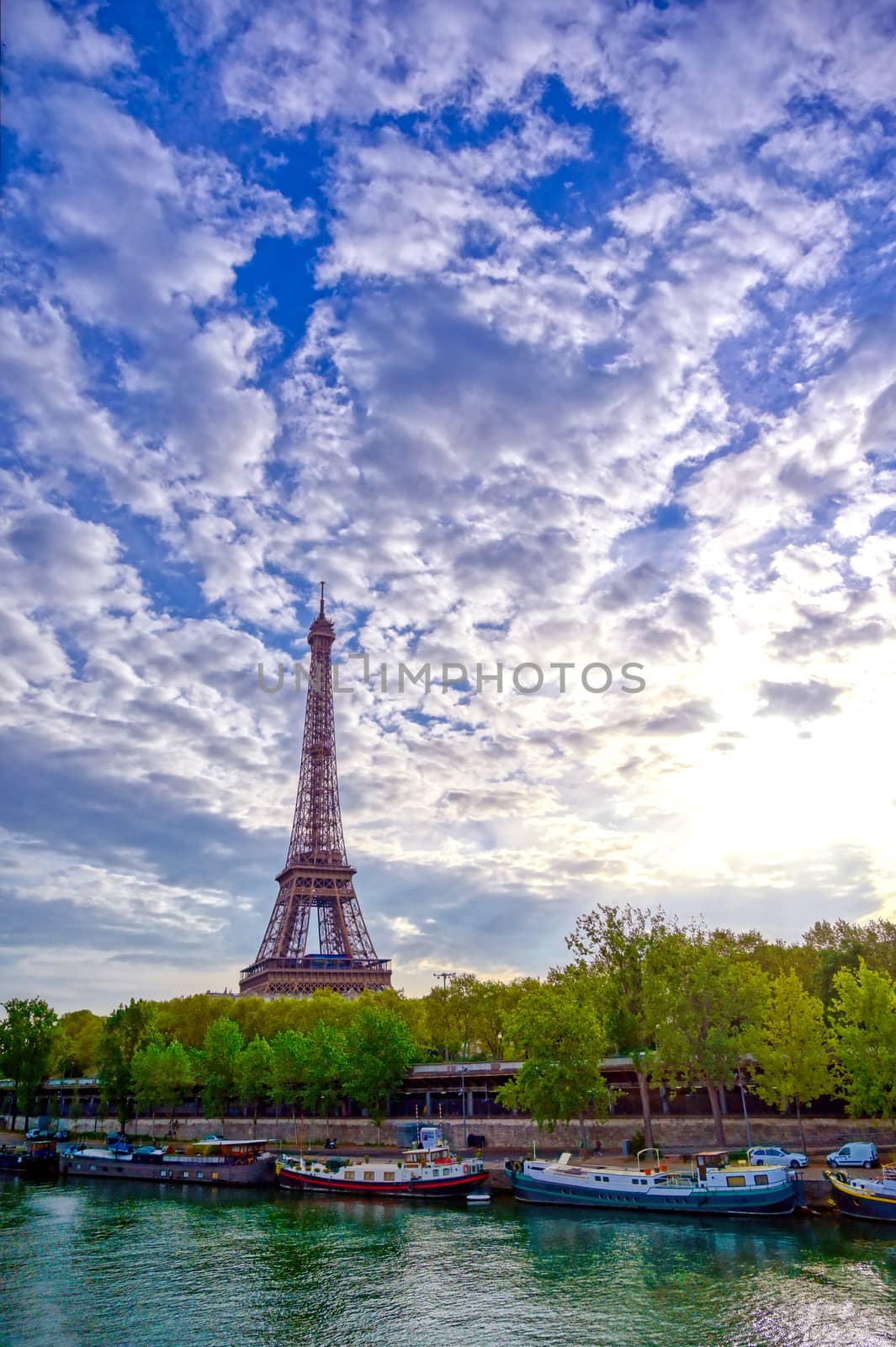 The Eiffel Tower across the Seine River in Paris, France on a sunny day with beautiful clouds.