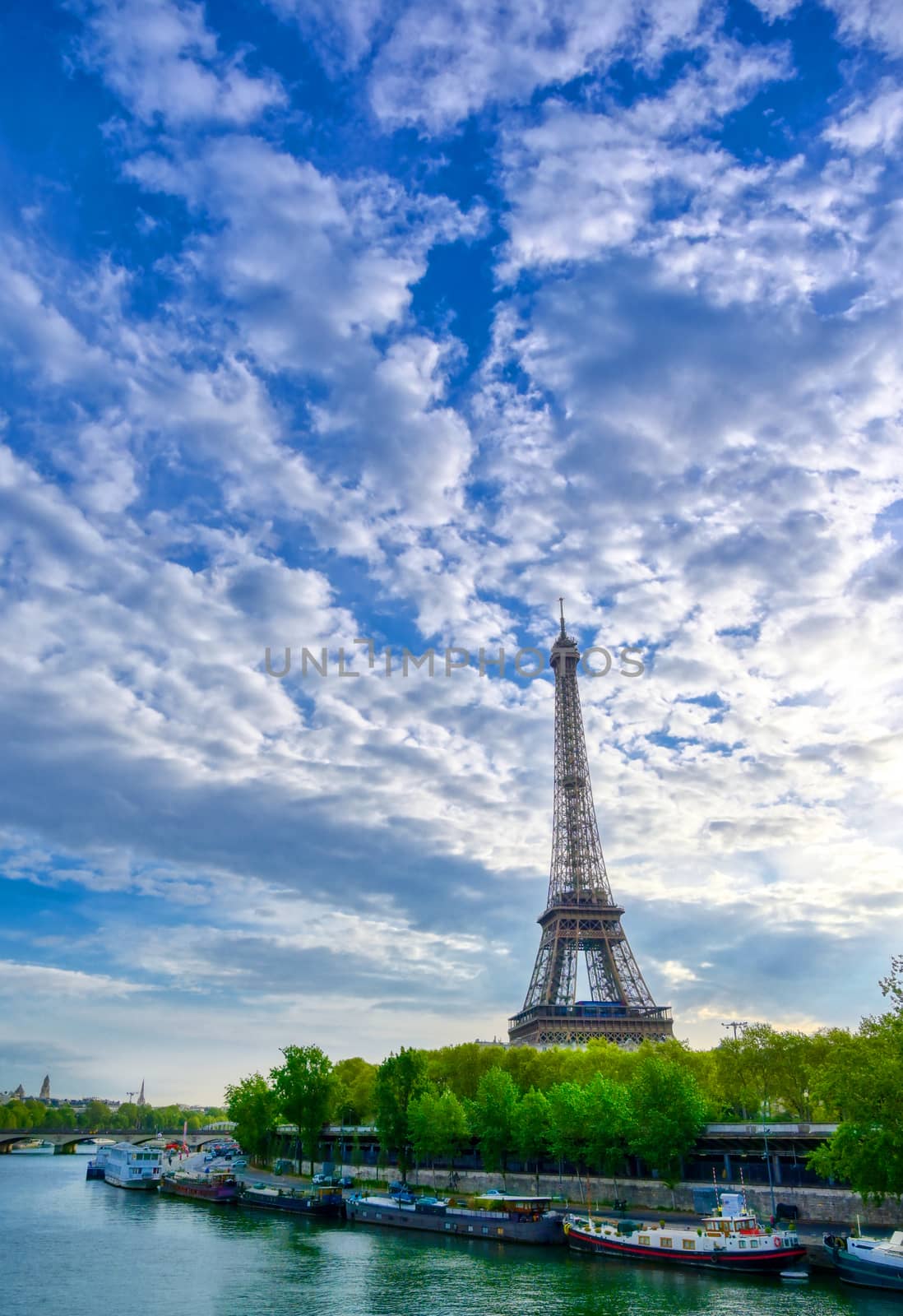 The Eiffel Tower across the Seine River in Paris, France on a sunny day with beautiful clouds.