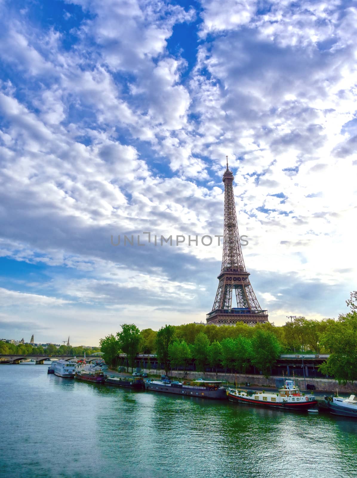 The Eiffel Tower across the Seine River in Paris, France on a sunny day with beautiful clouds.