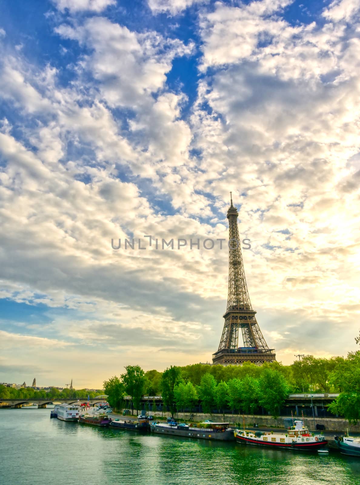 The Eiffel Tower across the Seine River in Paris, France on a sunny day with beautiful clouds.