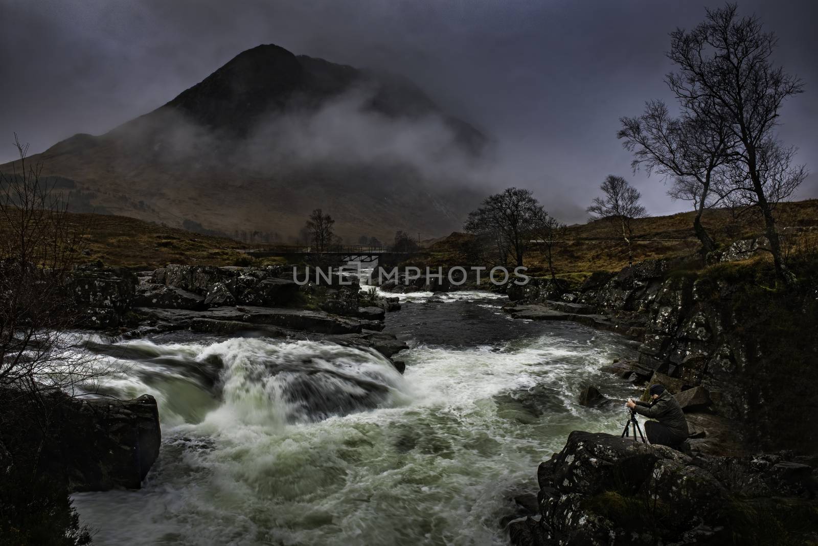 Glencoe, Scotland - Jan 2020: Photographer capturing water running over mountain wiers under the peaks at Glencoe in the Highlands of Scotland during winter 