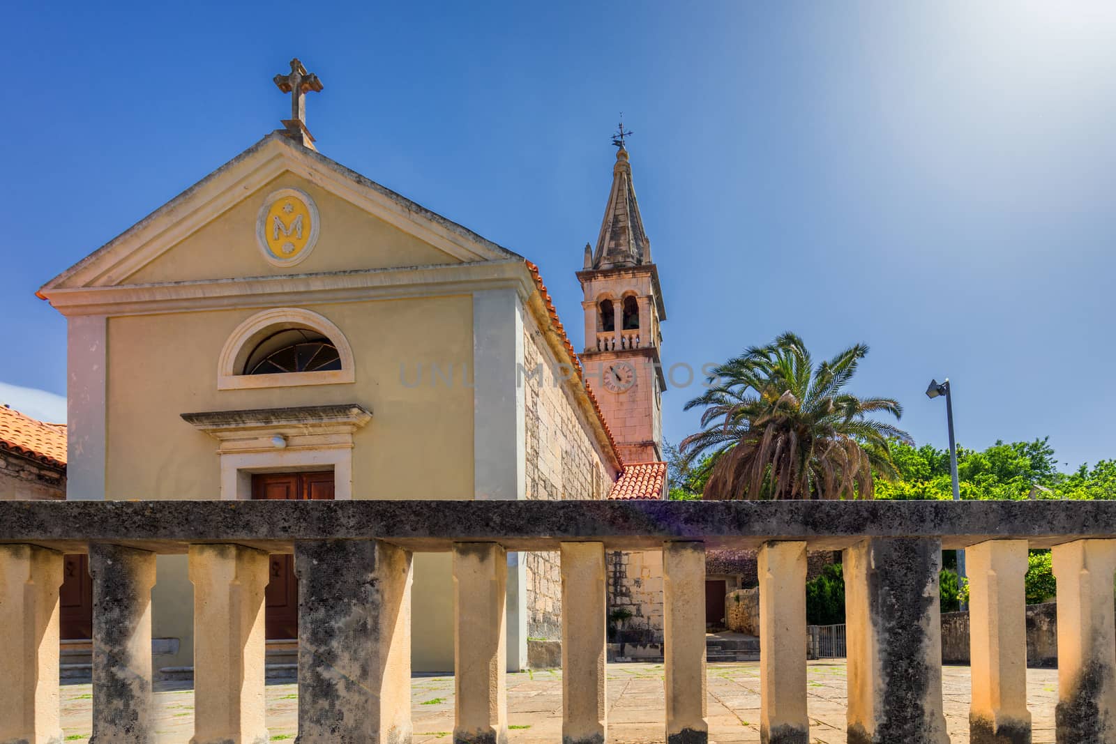 Church building and palm tree against sunny blue sky in Splitska village on Brac island, Croatia. 