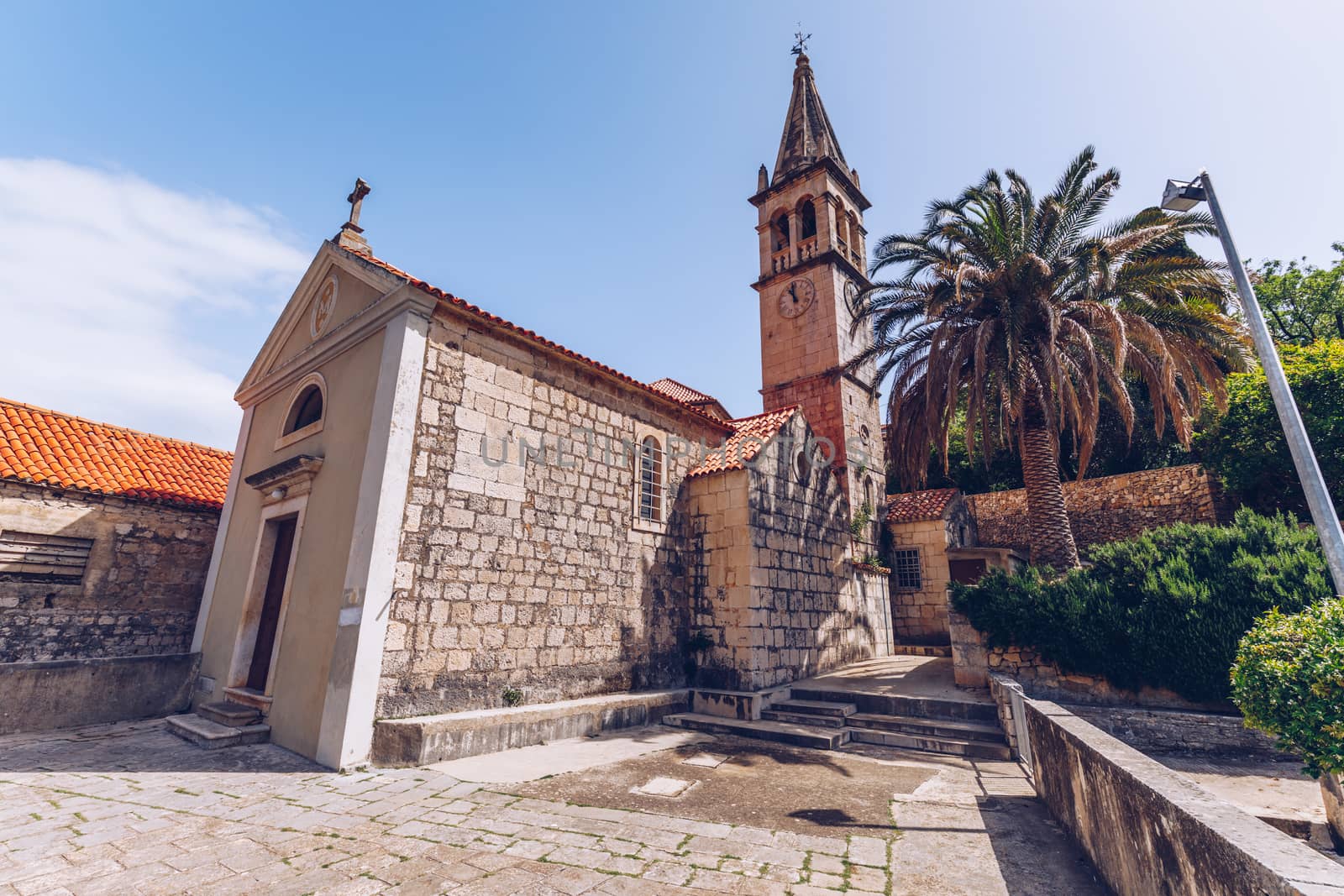 Church building and palm tree against sunny blue sky in Splitska village on Brac island, Croatia. 