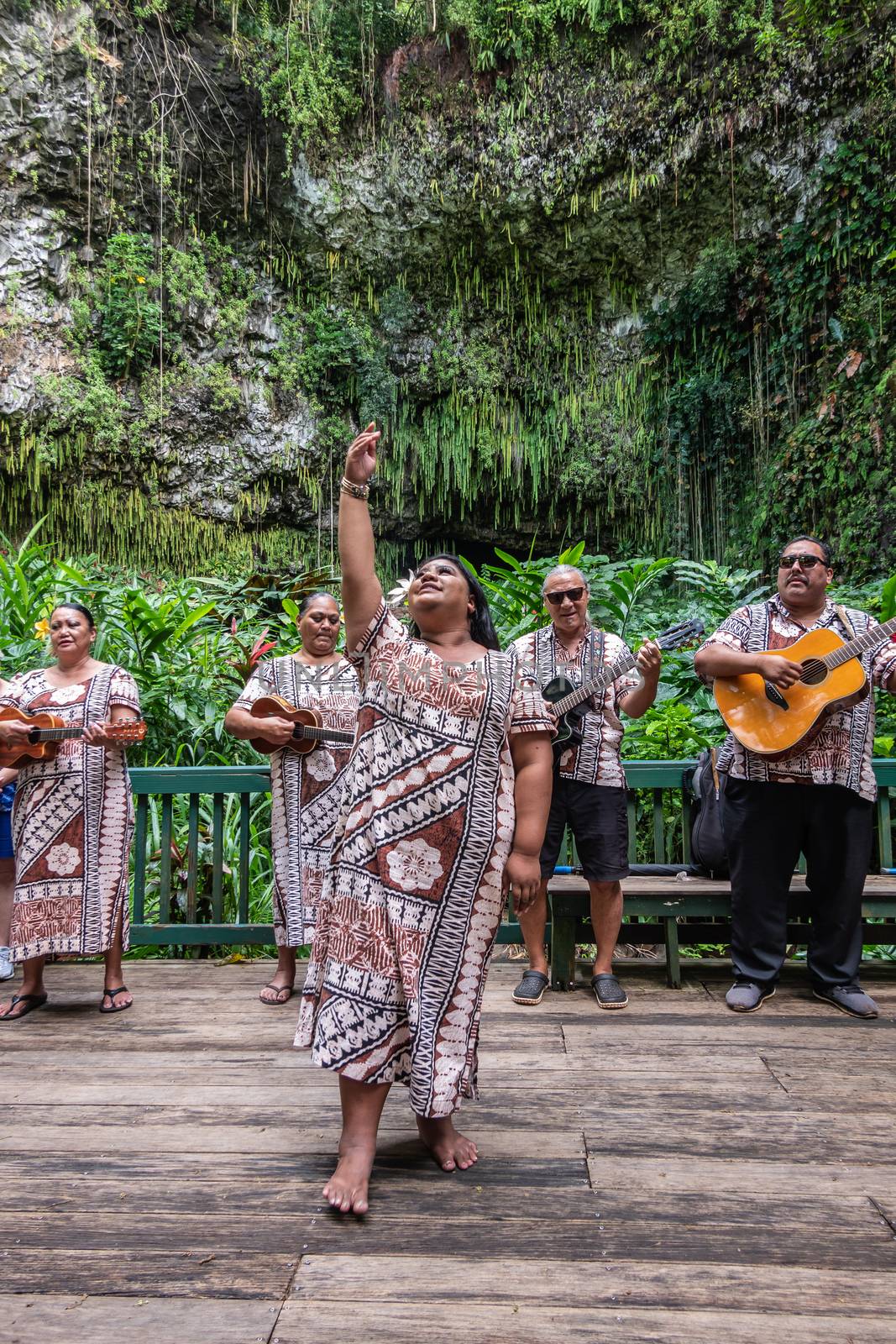 Kamokila Village, Kauai, Hawaii, USA. - January 16, 2020: Local folk band performs on stage in front of Fern Grotto. Female singer in front. Green background.