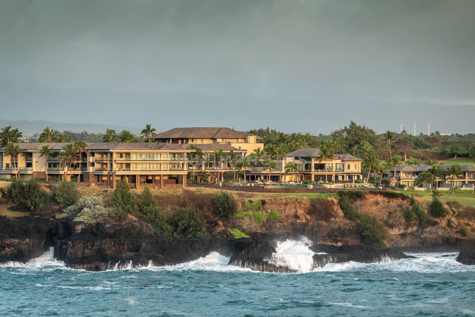 Nawiliwili, Kauai, Hawaii, USA. - January 16, 2020: Early morning light on Marriott resort behind green golf course under blueish gray sky. Blue ocean crashes white on black shoreline.