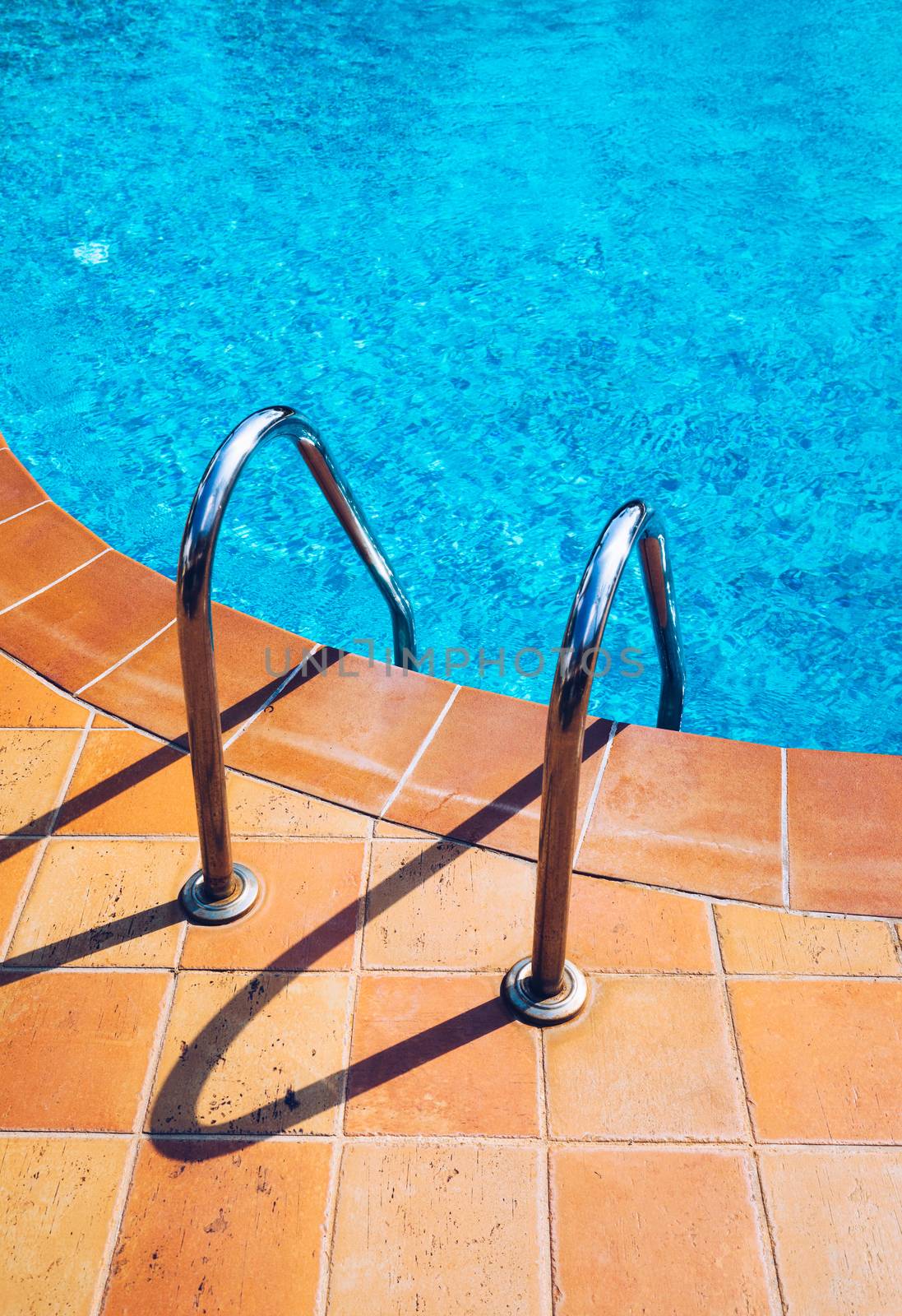 Swimming pool with stair. Grab bars ladder in the blue swimming pool. Poolside with blue clear water and ladder. Stair at the side of swimming pool, summer concept.