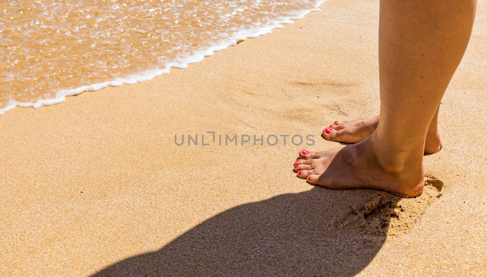 Closeup on leg of young woman standing on sea shore. Woman legs and feet walking on the sand of the beach with the sea water in the background. Woman standing on the beach with wave sea.
