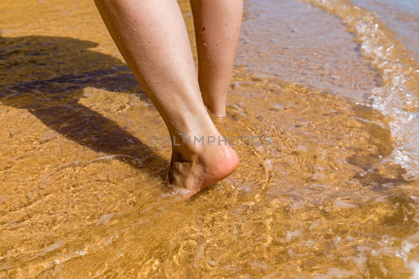 Woman walking barefoot on a beach. Close up leg of young woman walking along wave of sea water and sand on the summer beach. Travel Concept. Woman walking on sand beach leaving footprints in the sand.