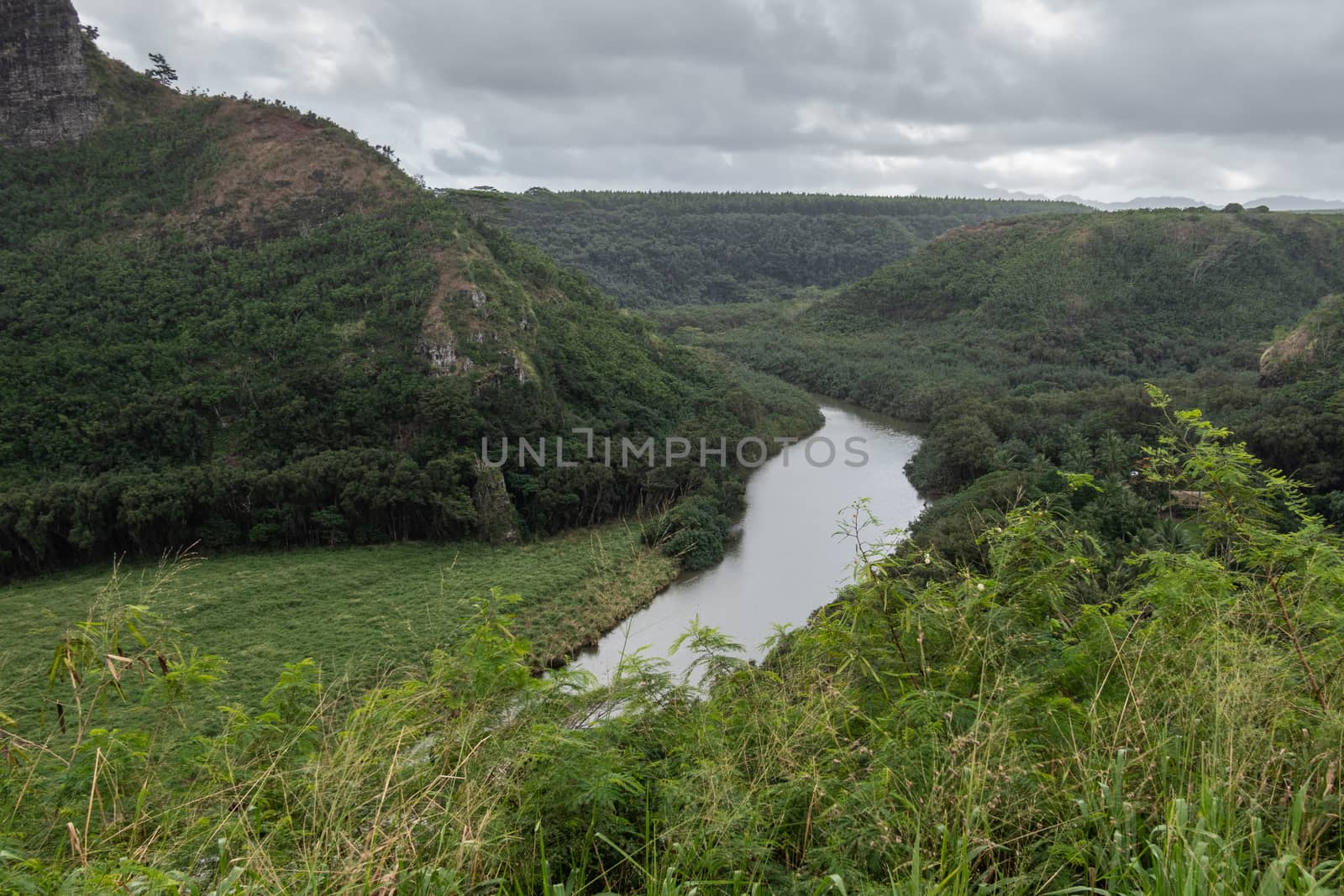 Nawiliwili, Kauai, Hawaii, USA. - January 16, 2020: Gray South Fork Wailua River meanders between green forested hills under gray rainy cloudscape.