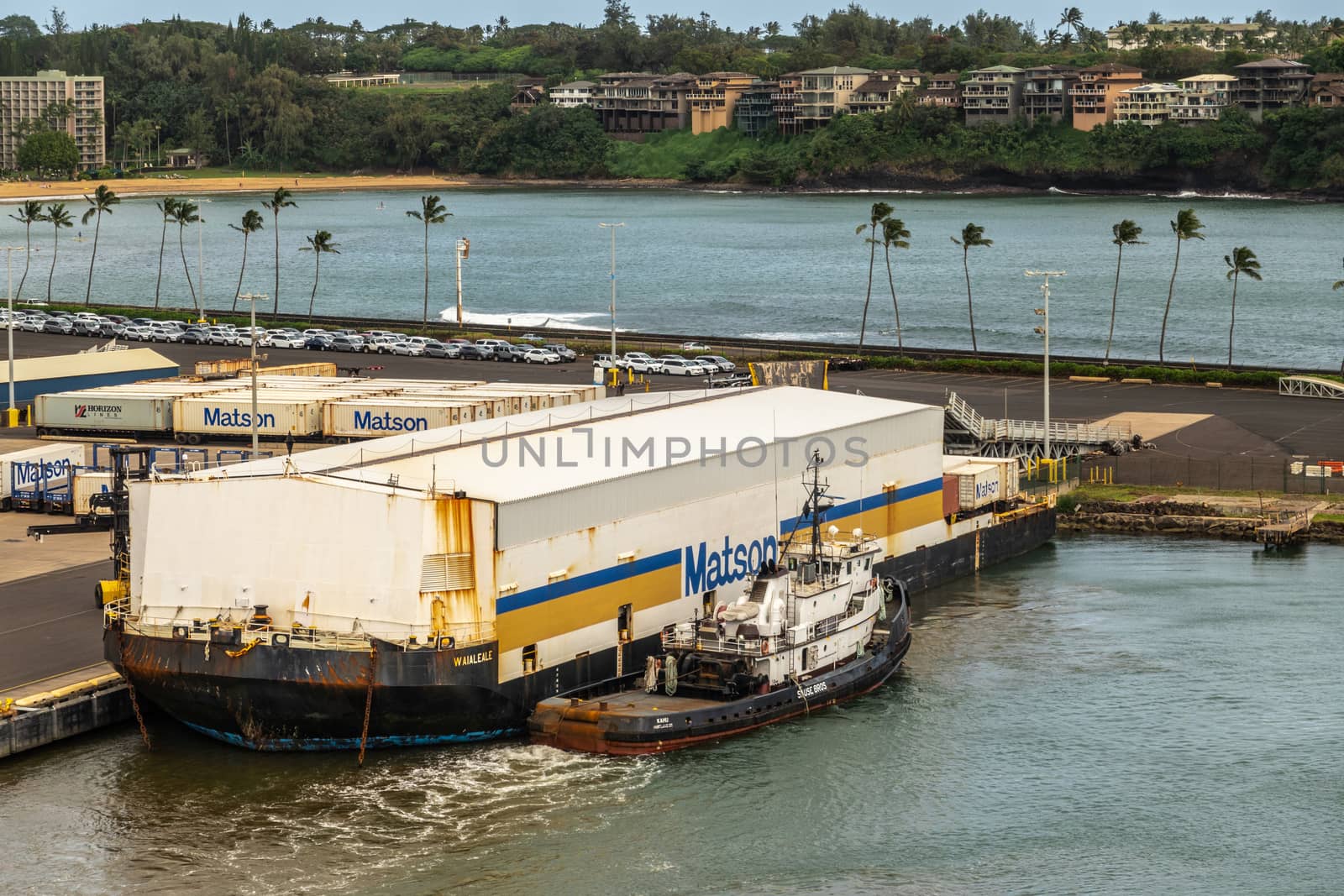 Nawiliwili, Kauai, Hawaii, USA. - January 17, 2020: Floating barge in port with white warehouse on top to cover shipping containers carries the Matson brand. Greenish ocean water. Green belt with housing.