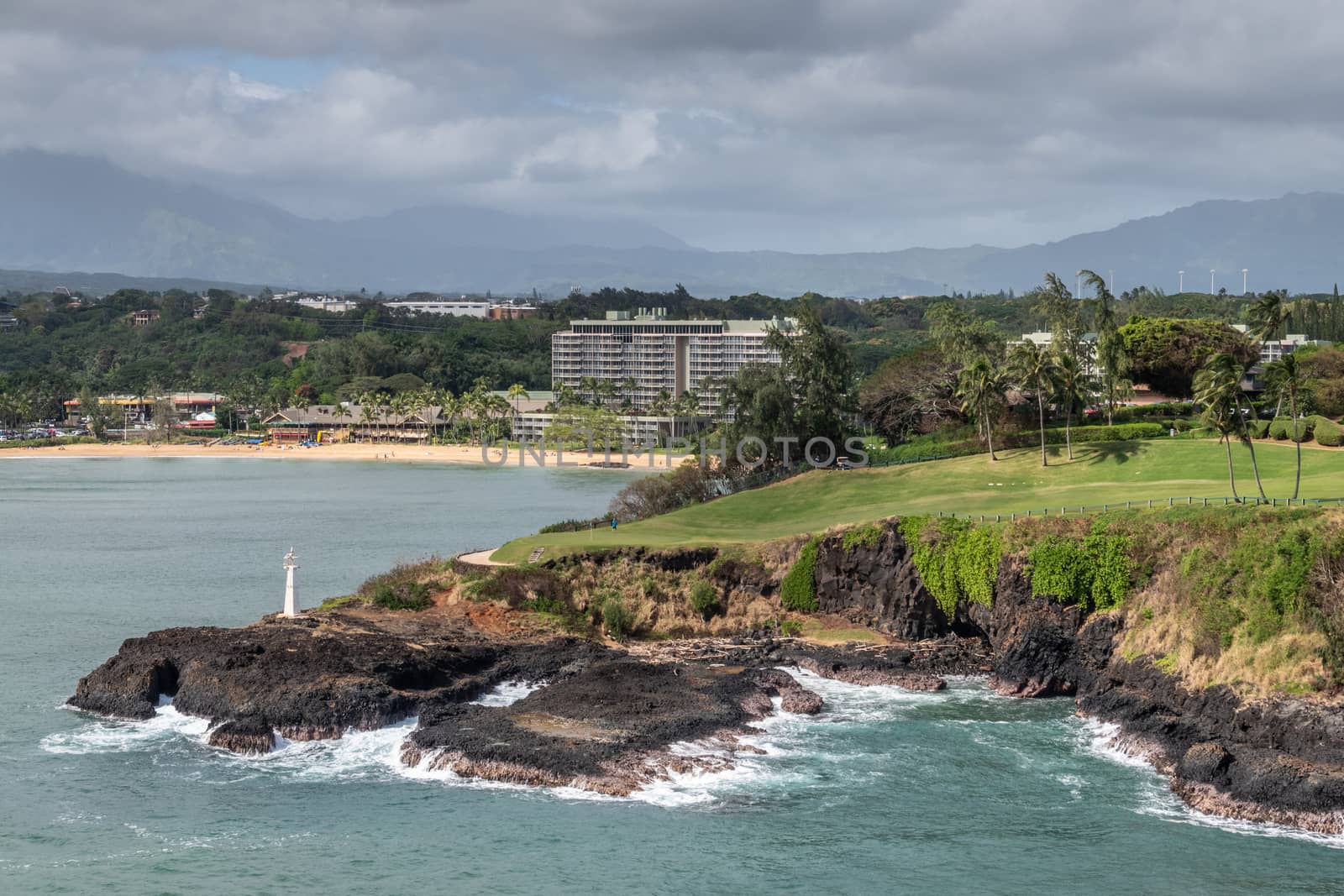 Nawiliwili, Kauai, Hawaii, USA. - January 17, 2020: Wide view over Marriott beach resort, green golf course with Kukii lighthouse or beacon on black lava rock up front. Greenish ocean water., Cloudscape.