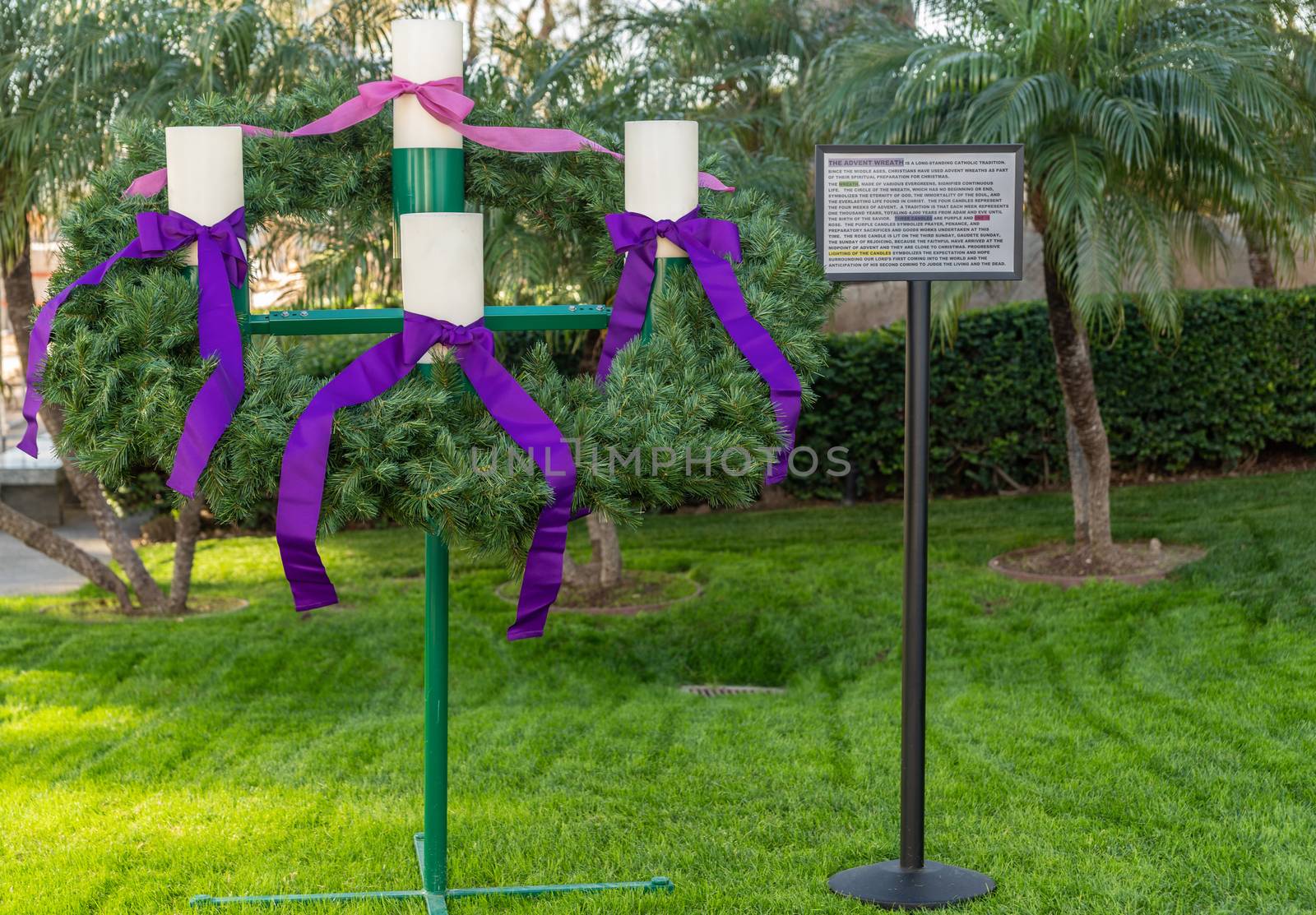 Garden Grove, California, USA - December 13, 2018: Crystal Christ Cathedral. Closeup of the Advent Wreath in the garden with explaining poster. Green backgroound, four white candles, purple and pink ribbons.
