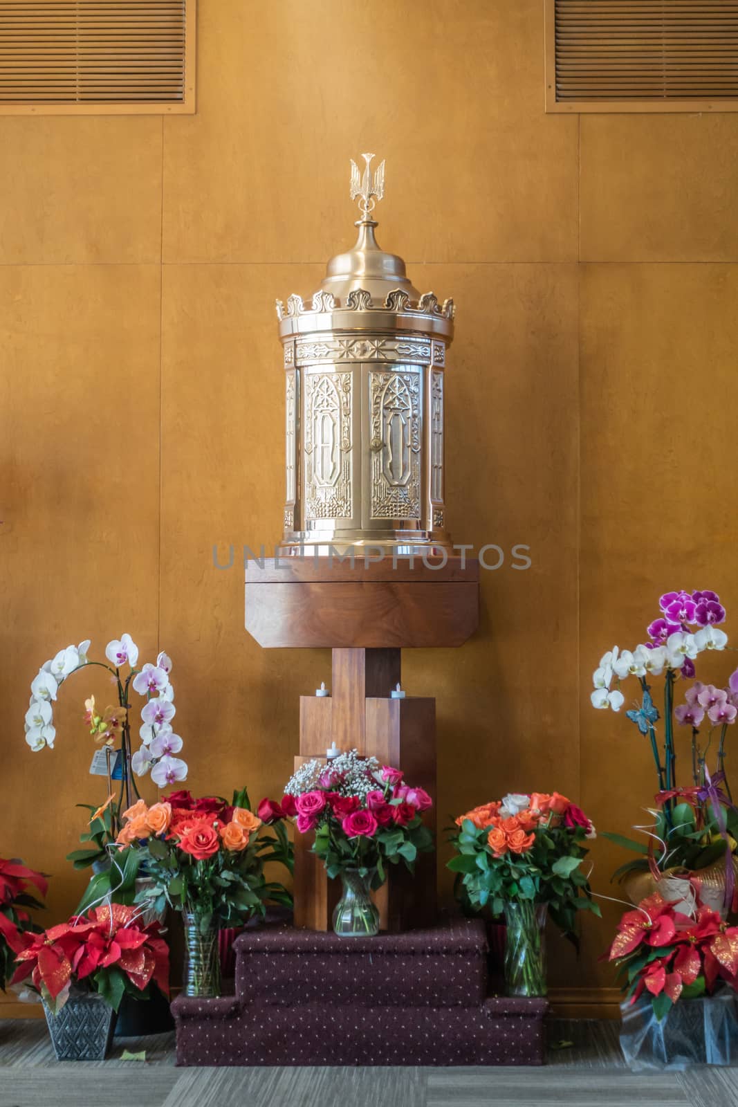 Garden Grove, California, USA - December 13, 2018: Crystal Christ Cathedral. Golden tabernacle in Blessed Sacramet Chapel against brown wooden wall. Many flowers up front.