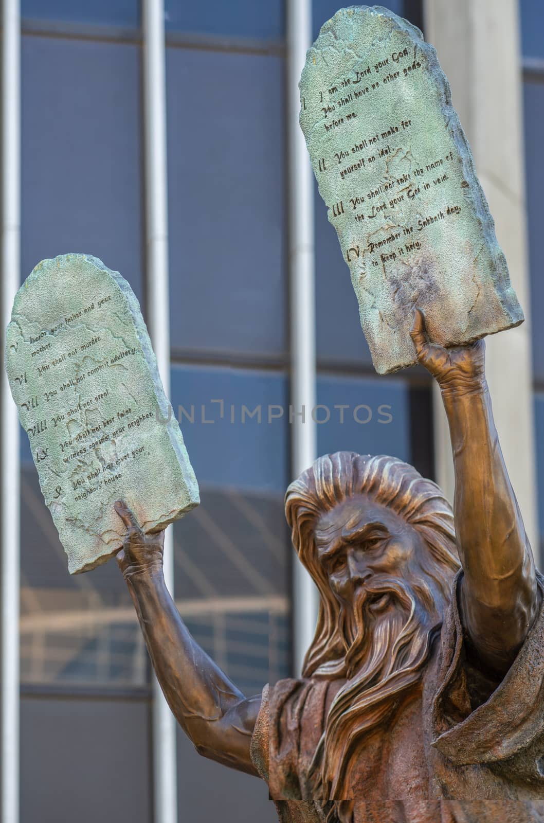 Garden Grove, California, USA - December 13, 2018: Crystal Christ Cathedral. Closeup of Bronze statue of Moses putting the ten commandments of two tables in the air. Some green foliage, facade of Tower of Hope.