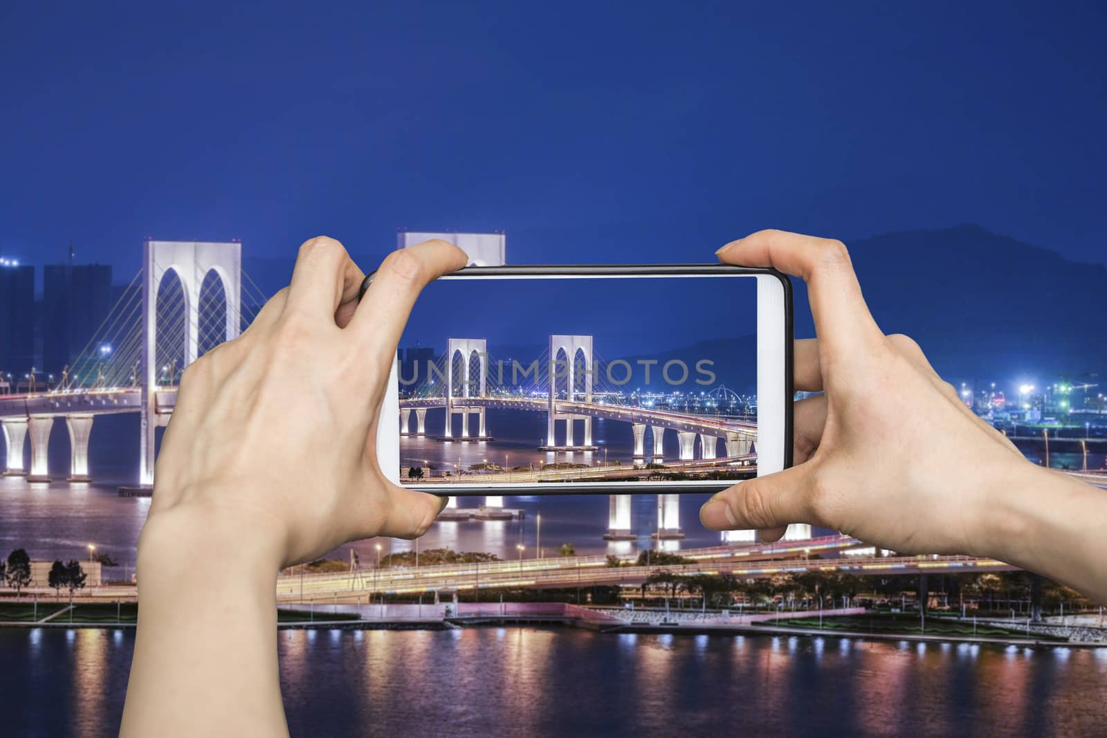 Girl taking pictures on mobile smart phone in View point Bridge in Macau at night