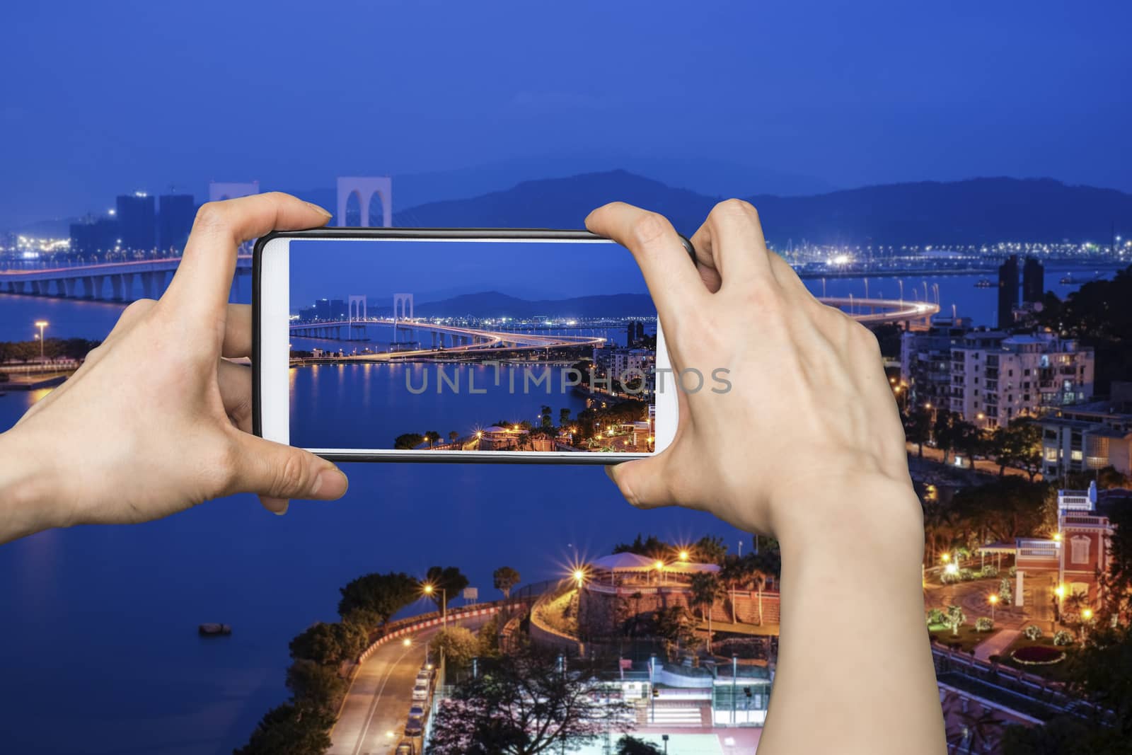 Girl taking pictures on mobile smart phone in View point Bridge in Macau at night