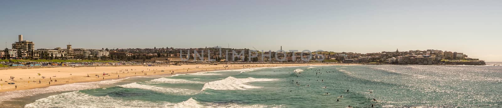 Sydney, Australia - February 11, 2019:  Panorama shot of sandy Bondi beach part and its north shore with housing and nature reserves. Blue water and sky.