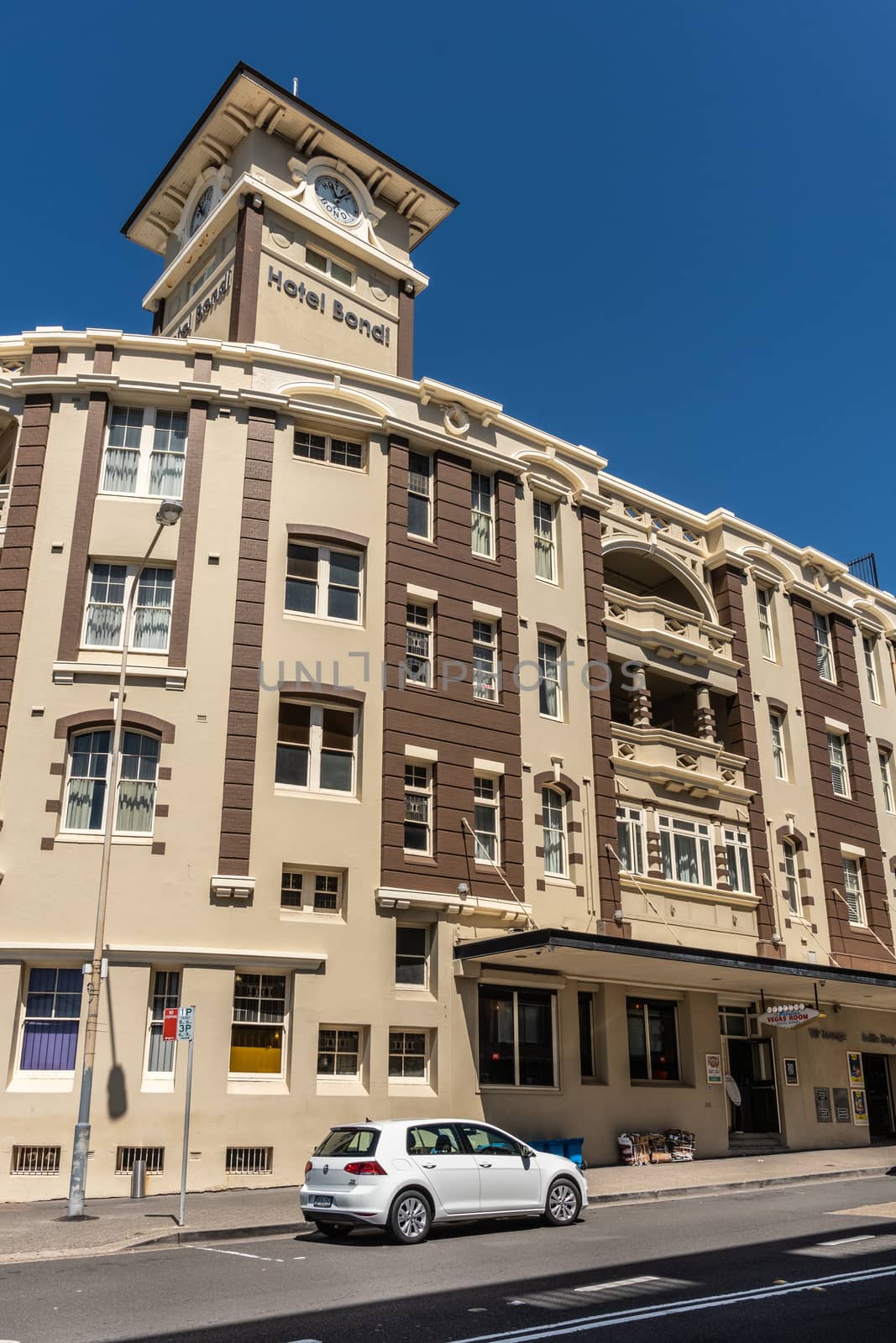 Sydney, Australia - February 11, 2019: Yellow and brown Bondi Hotel facade under blue sky in Bondi Beach. Street scene with parked car.