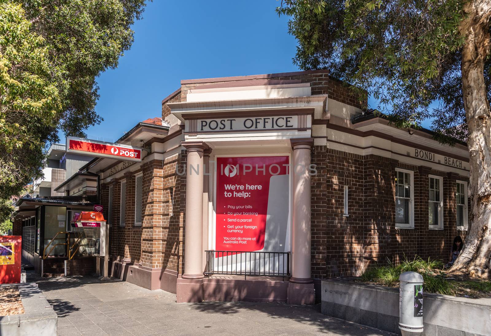 Sydney, Australia - February 11, 2019: Post Office building of Bondi Beach. Street scene with green vegetation. White on red advertisements on columned facade.