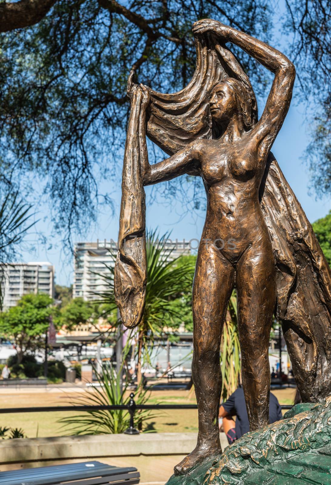Sydney, Australia - February 11, 2019: Closeup of part of Salvador Dali statue copy in First Fleet Park near Circular Bay, labeled Nobility of Time, set under green tree foliage with the bay and its buildings in back.