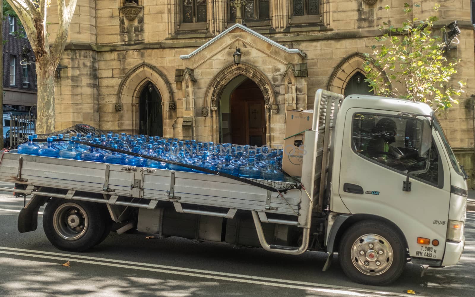 Sydney, Australia - February 12, 2019: White flatbed van transports a full load of blue large drinking water bottles. Back is yellow facade of Saint Patricks Church.