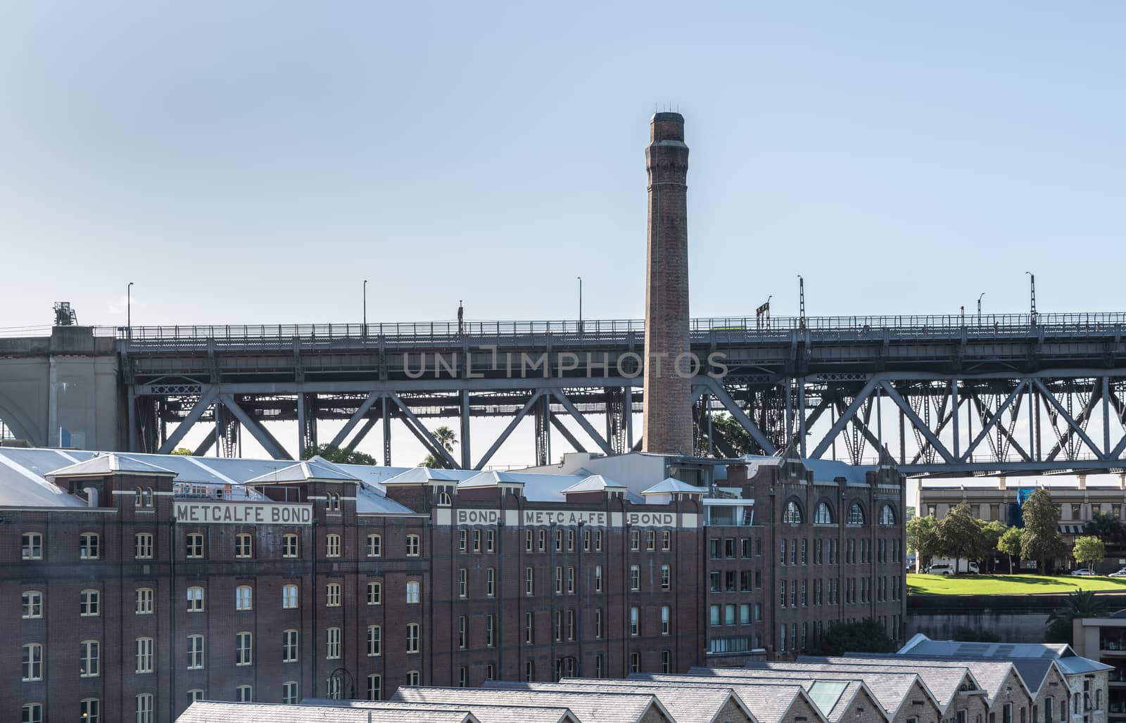 Sydney, Australia - February 12, 2019: Historic harbor warehouses with tall chimney sports Metcalfe Bond advertisement on facade. At foot of Harbour bridge.