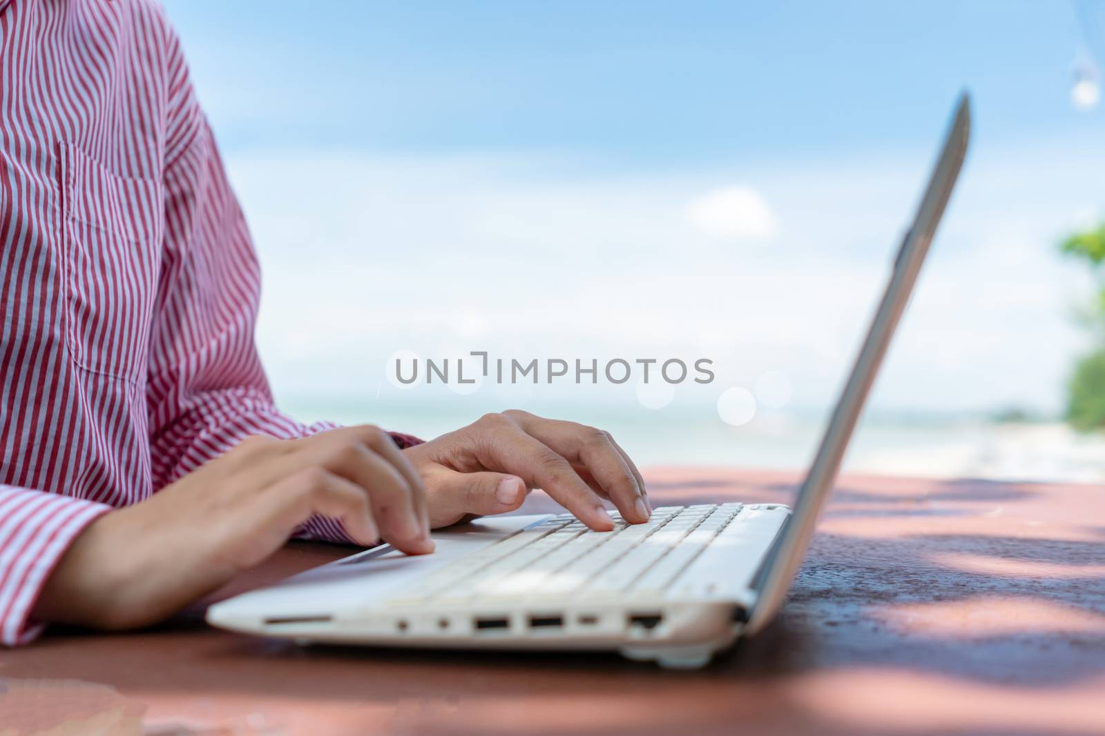 Woman hand using laptop to work study on work desk with clean nature beach outdoor background. Business, financial, trade stock maket and social network concept.