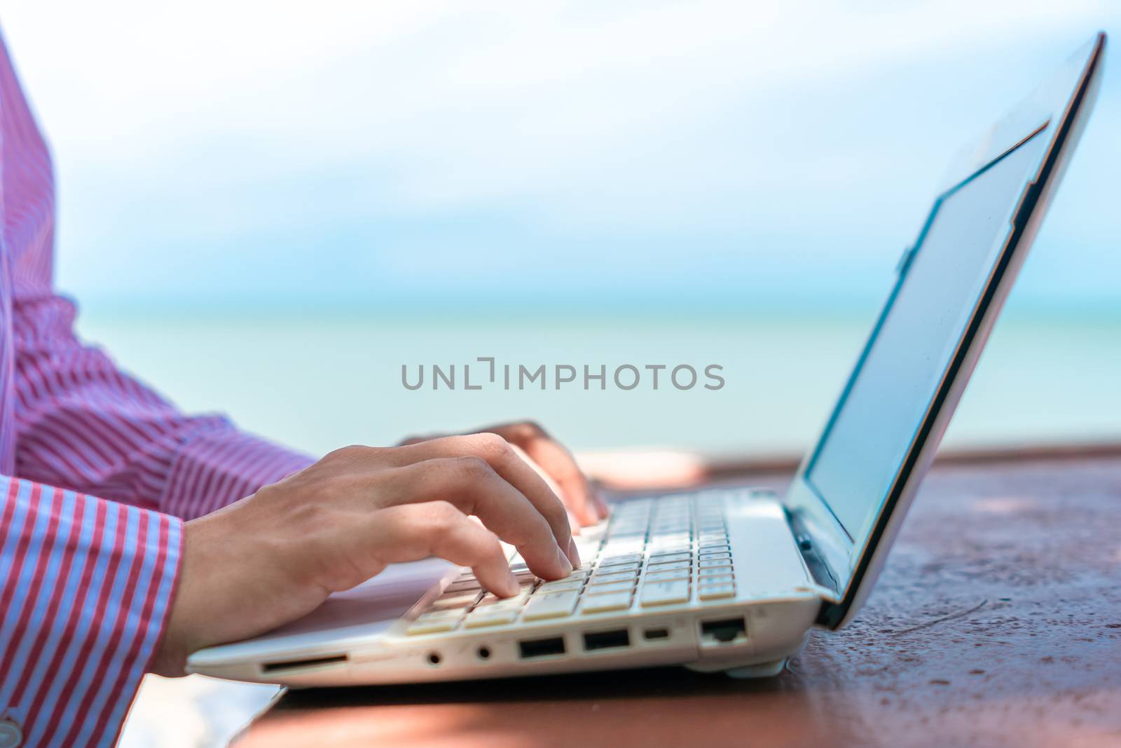 Woman hand using laptop to work study on work desk with clean nature beach outdoor background. Business, financial, trade stock maket and social network concept.