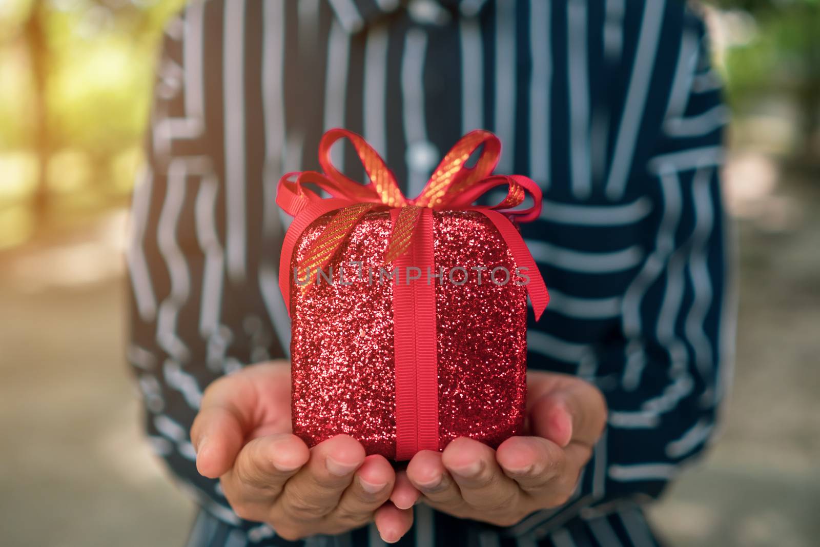 Hand hold gift box to someone on green bokeh nature. Celebration holiday concept.