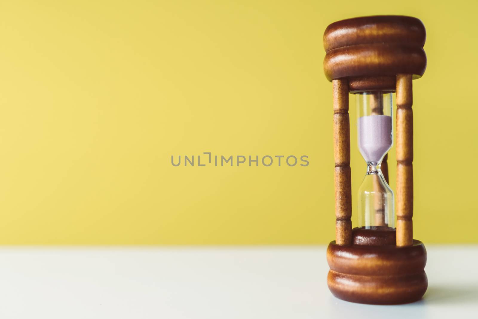 Selective focus of wooden hourglass on yellow background. Time and life concept.