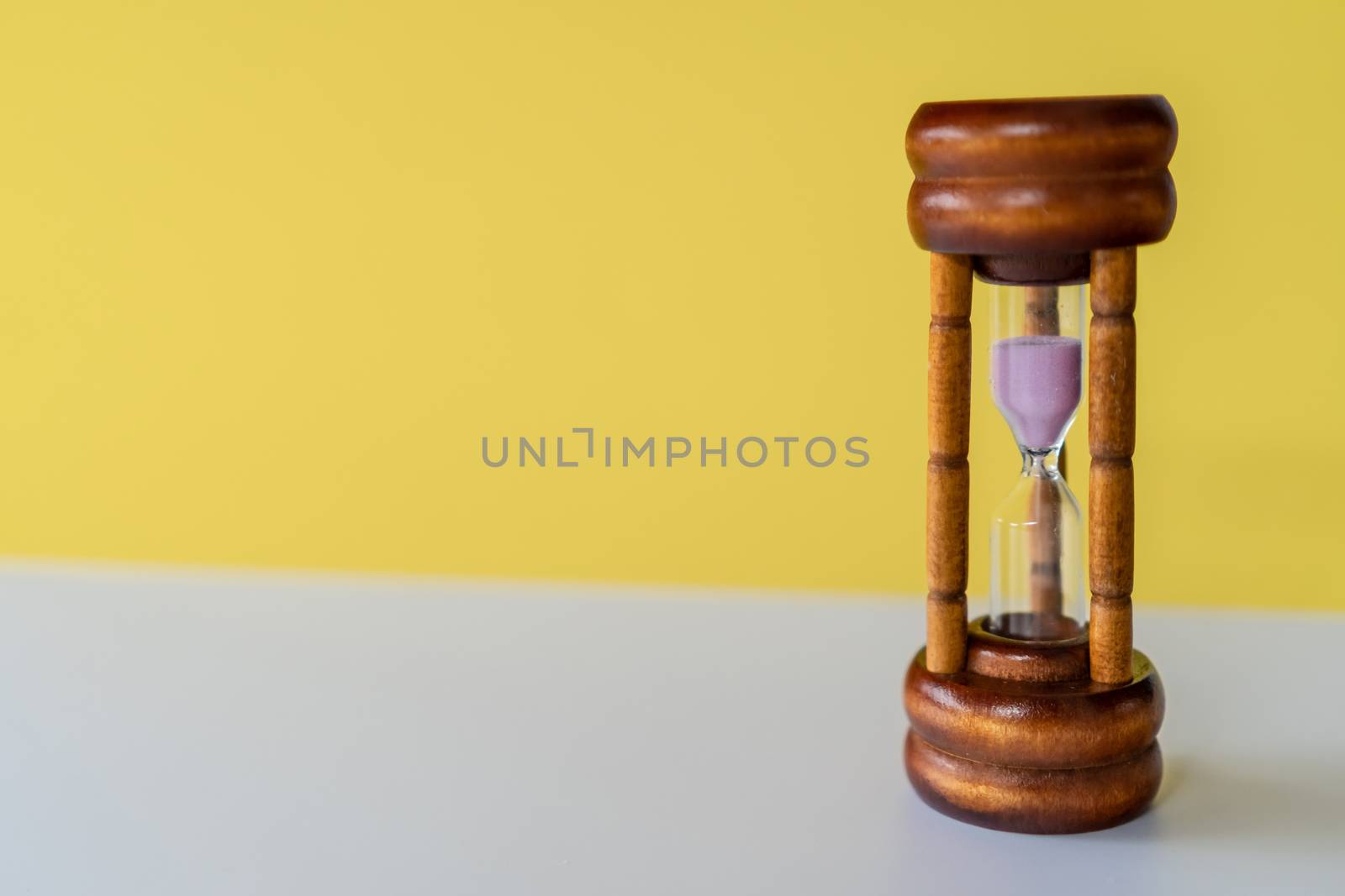 Selective focus of wooden hourglass on yellow background. Time and life concept.