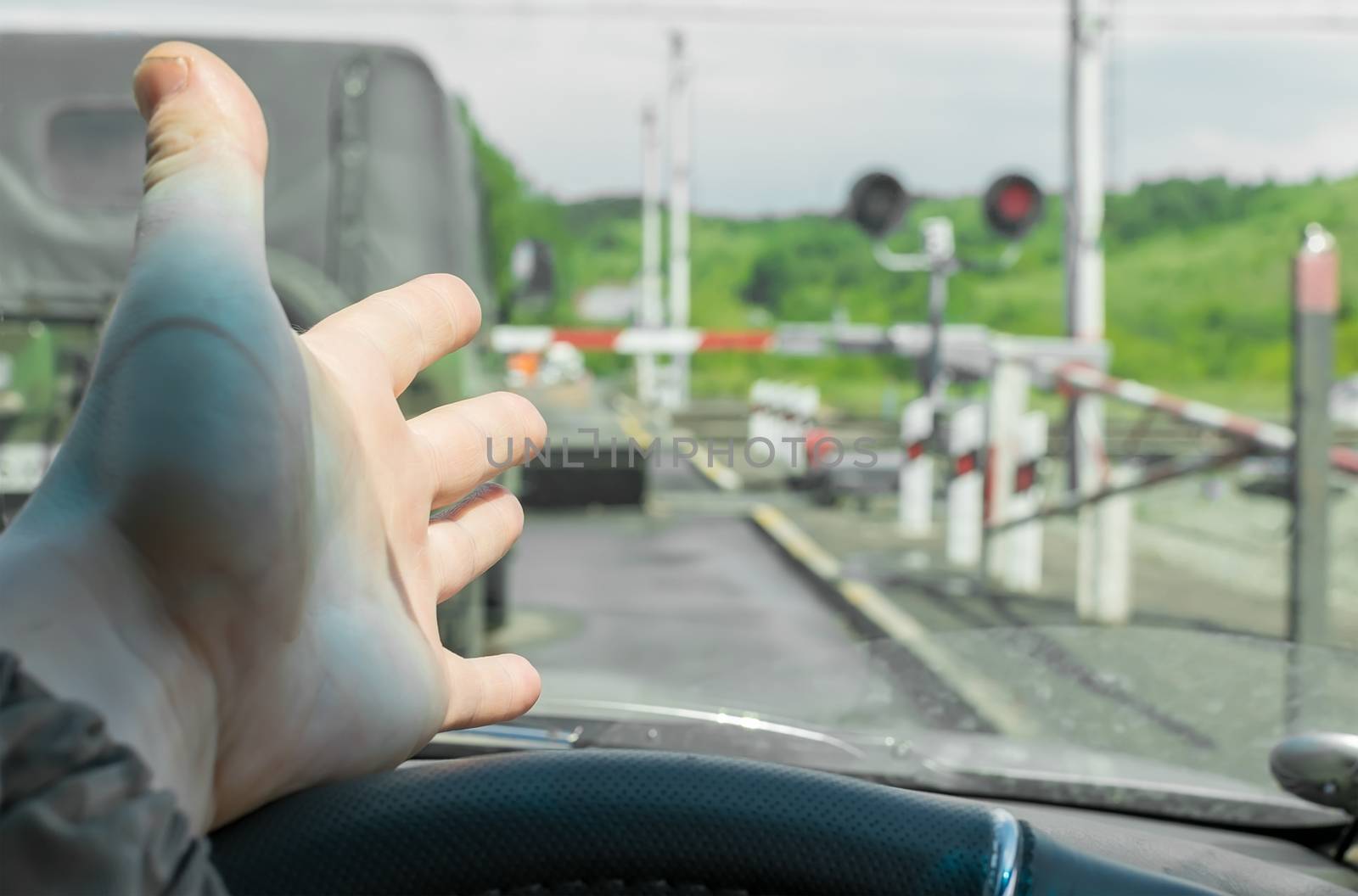 The hand of man inside the car. The car stopped in front of a closed barrier and a red traffic light before the railway crossing. Man outraged by the situation that did not have time to ride the move