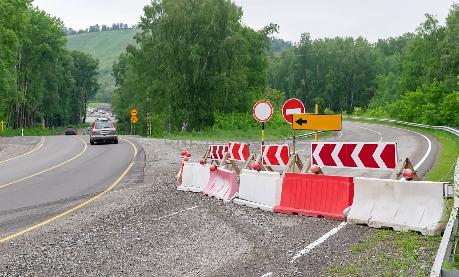 view of a fenced road closed for repairs against the background of passing cars on the bypass