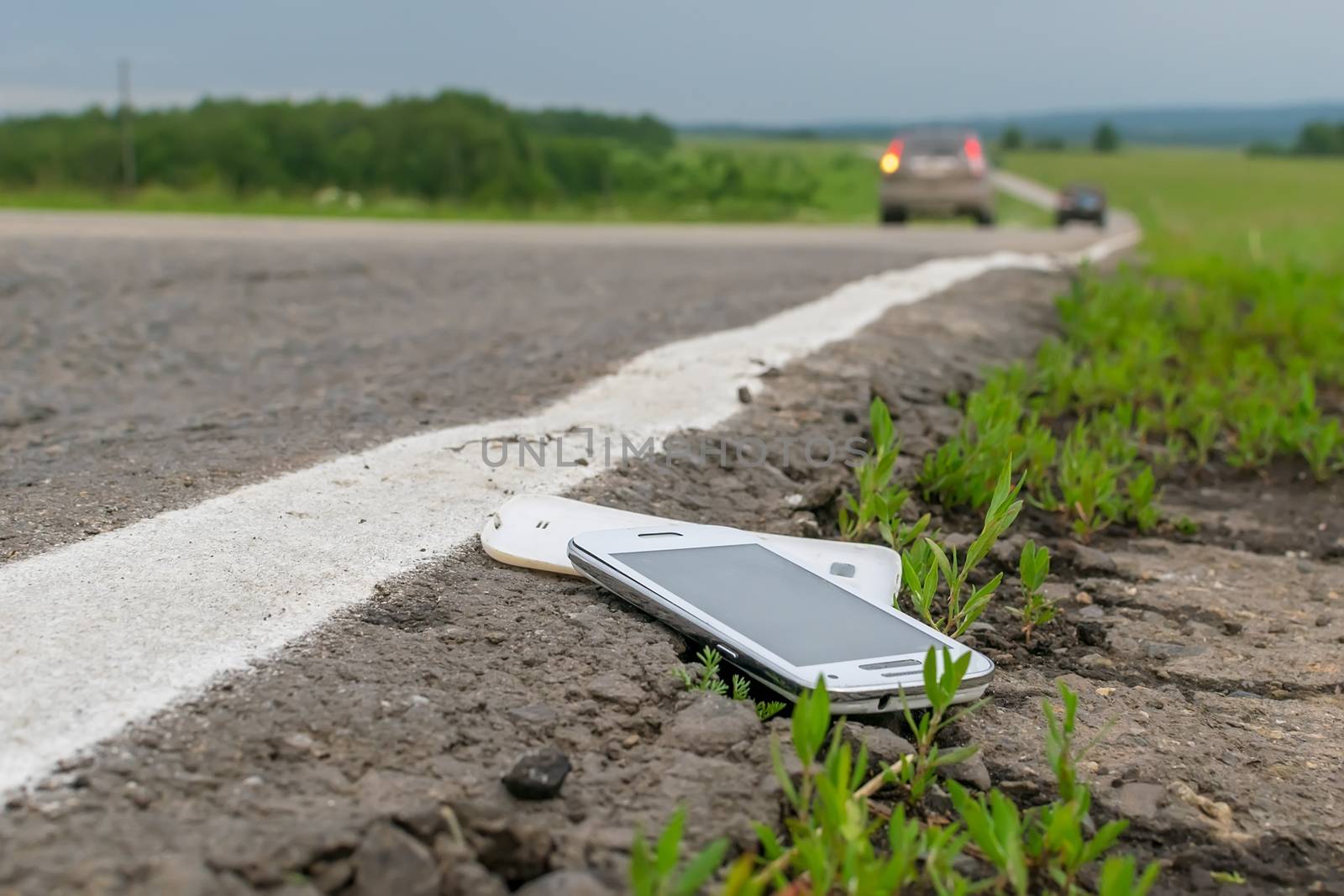 View of a mobile phone lying on the asphalt on a country road in cloudy weather