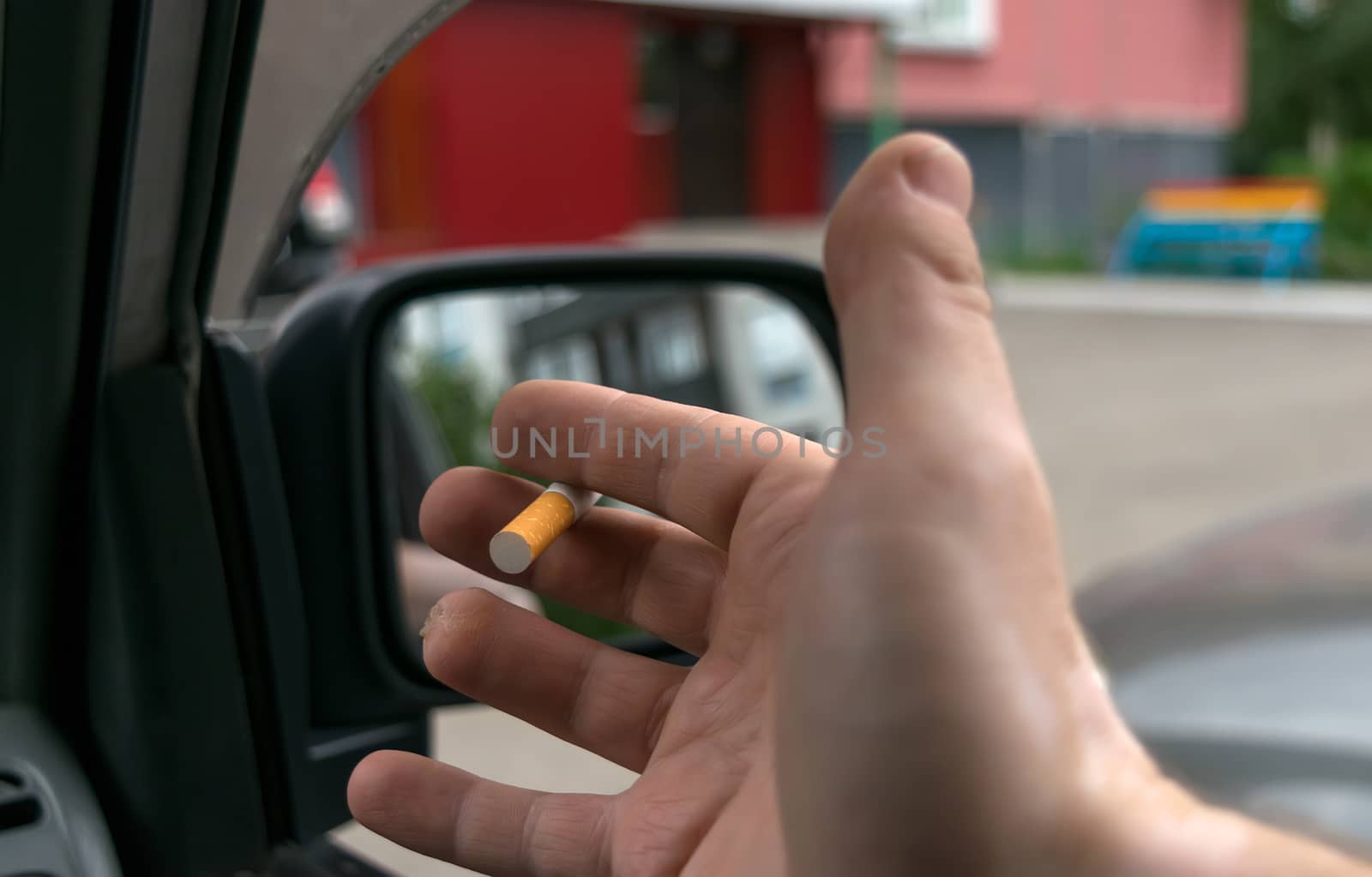close-up of a cigarette in the hand of a man in the car, who watches the entrance door of the house