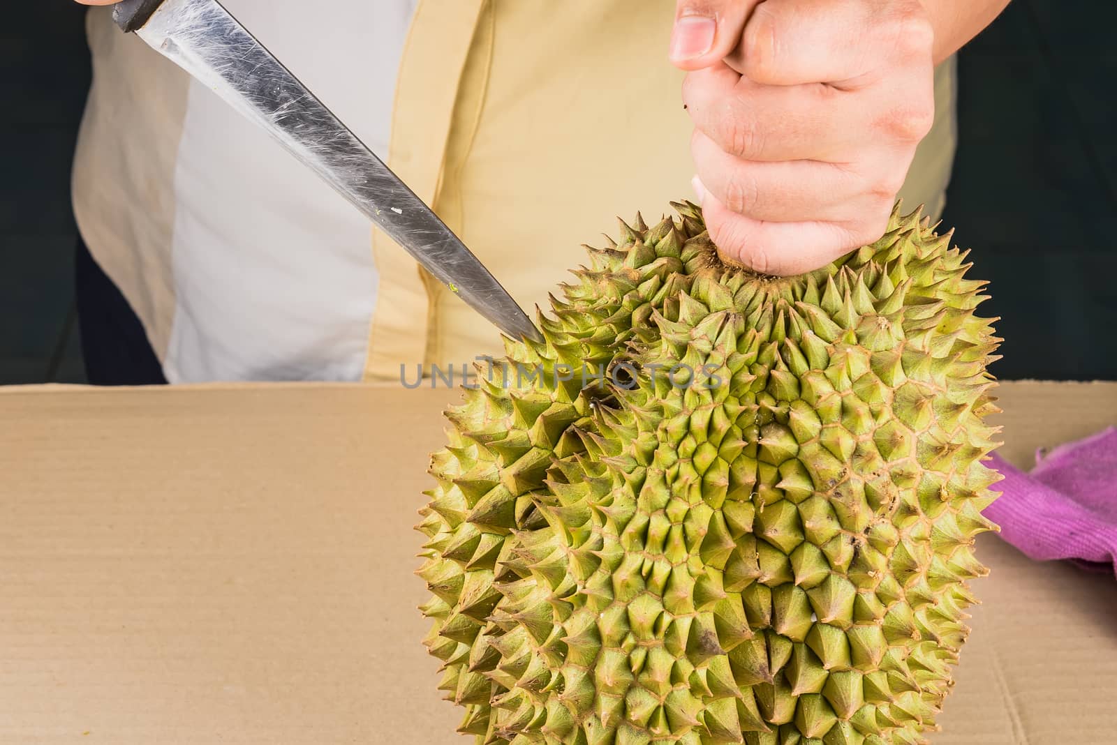 Woman cutting a Durian fruit on the wooden table by using a knif by Bubbers