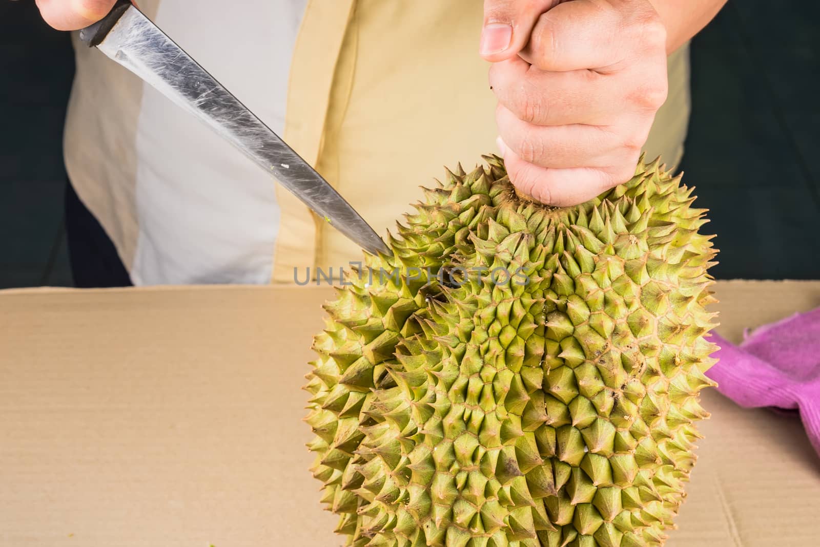 Woman cutting a Durian fruit on the wooden table by using a knife close up. Durian is the one of popular fruit in Thailand.