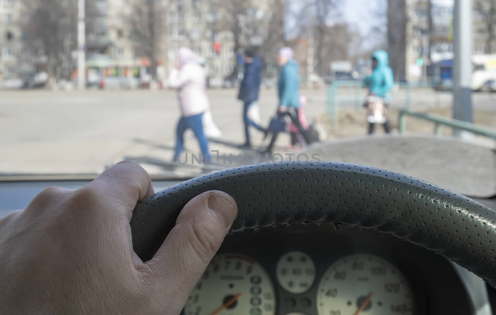 view from the car, the man's hand on the steering wheel of the car, located opposite the pedestrian crossing and pedestrians crossing the road