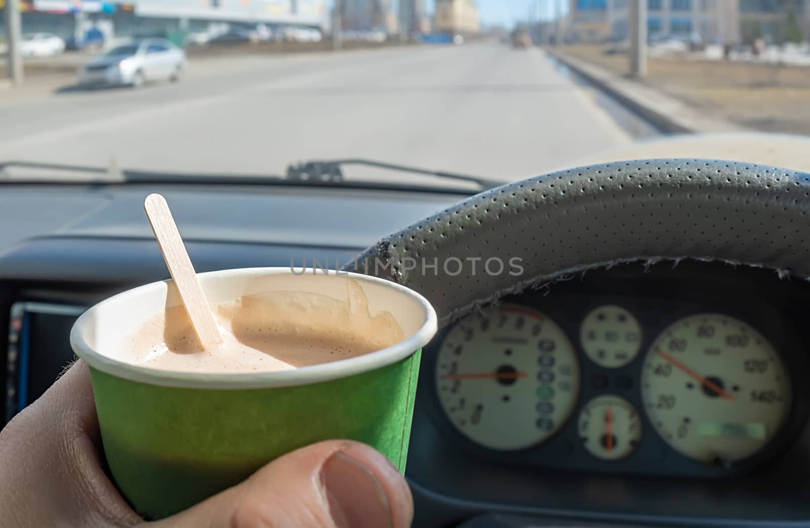 view of a glass of cocoa, chocolate, hot drink in the hand of a driver who is driving a car that is moving along a city street at speed