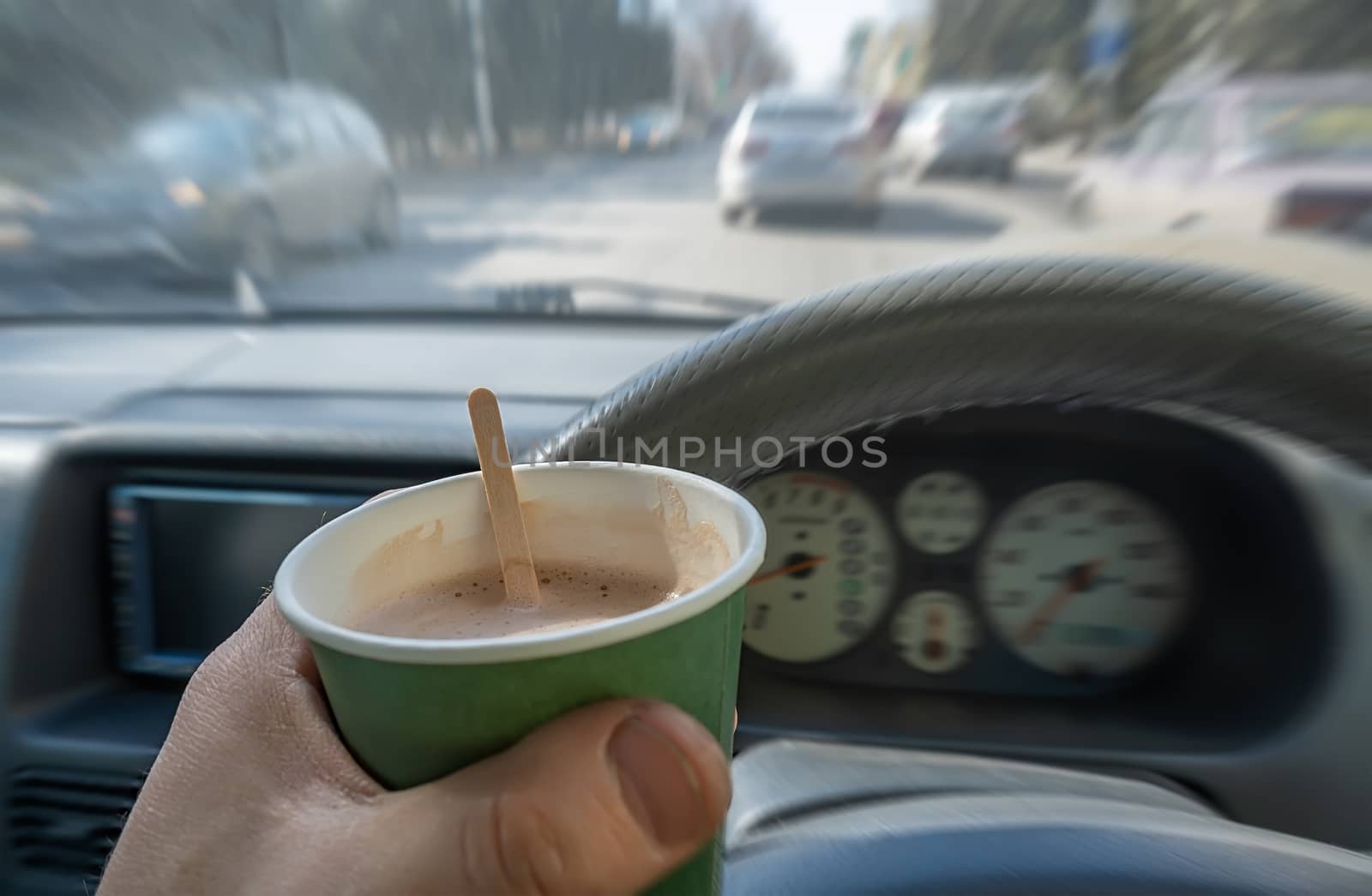 view of a glass of cocoa, chocolate, hot drink in the hand of a driver who is driving a car that is moving along a city street by jk3030