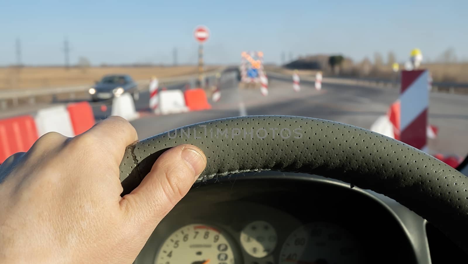 the driver hand on the steering wheel of a car that passes along a highway that is fenced with signal signs by jk3030