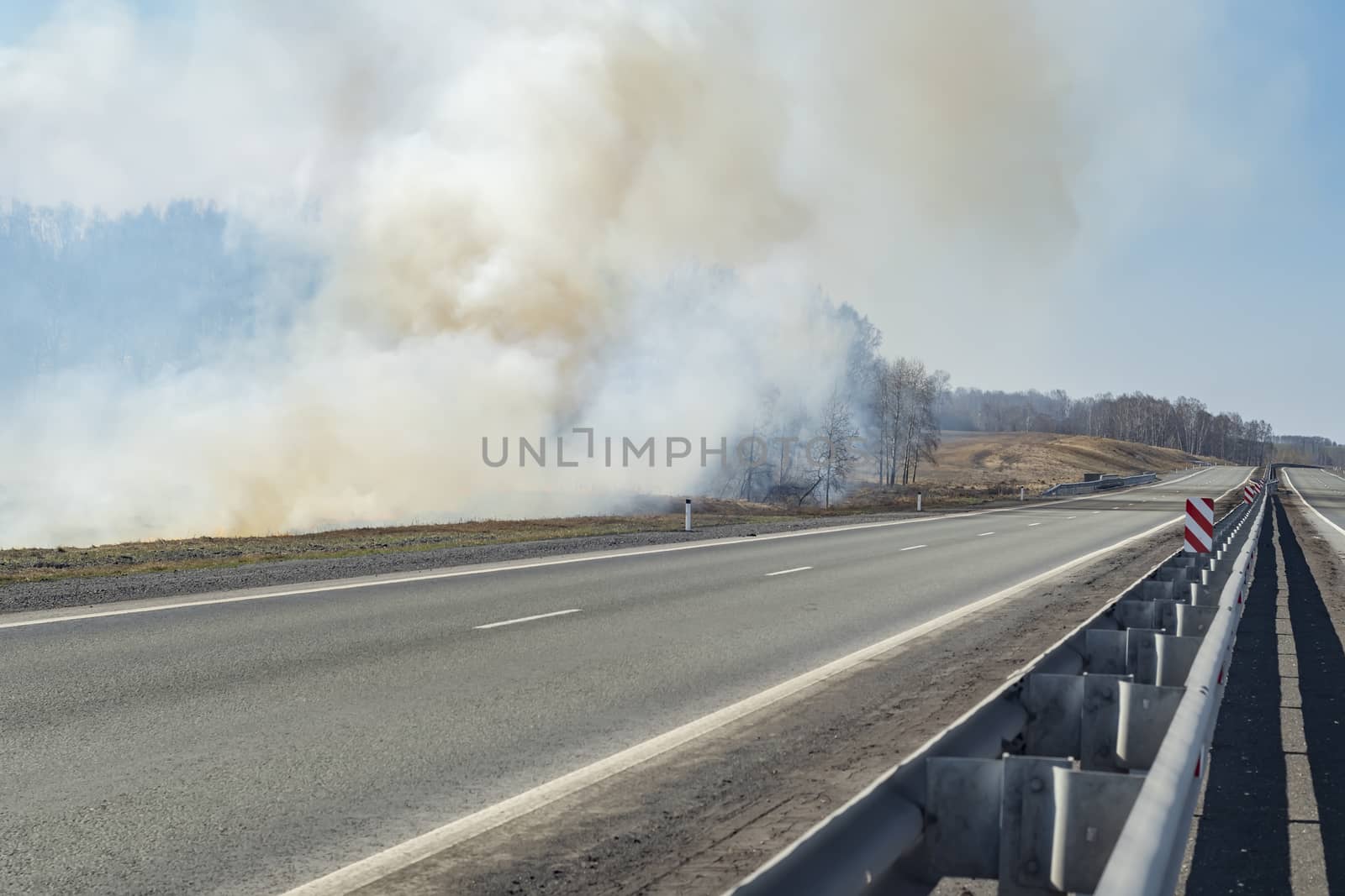 a strong fire, flame and a lot of smoke near the paved highway route, burning dry grass