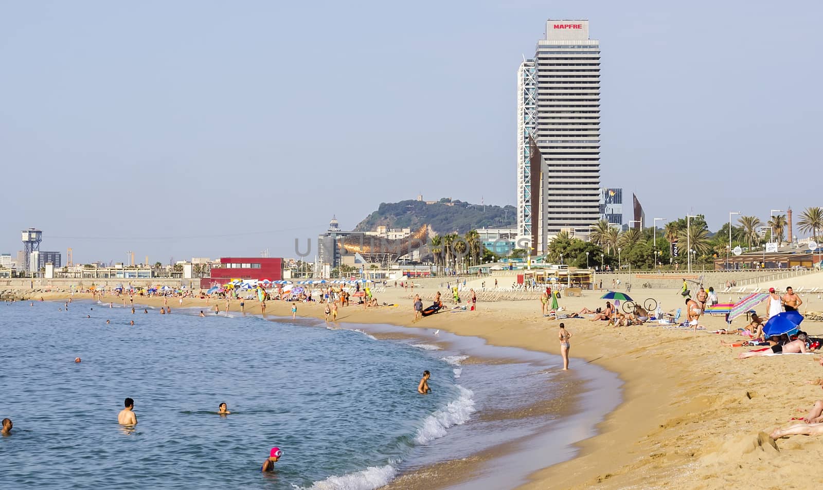 BARCELONA, SPAIN - JULY 5, 2015: Barceloneta Beach and skyscraper Torre Mapfre in the Olympic Port. It is named after its owner, Mapfre, an insurance company. This tower holds the title for highest helipad in Spain at 505 feet above ground.

Barcelona, Spain - July 5, 2015: Barceloneta Beach and skyscraper Torre Mapfre in the Olympic Port. It is named after its owner, Mapfre, an insurance company. This tower holds the title for highest helipad in Spain at 505 feet above ground. People are resting on the beach.