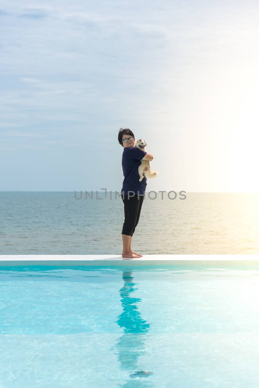 Asian woman and dog happy smile hugging at outdoor swimming pool seaside turquoise sea or ocean with horizon of blue sky at resort or hotel when vacation travel for relax