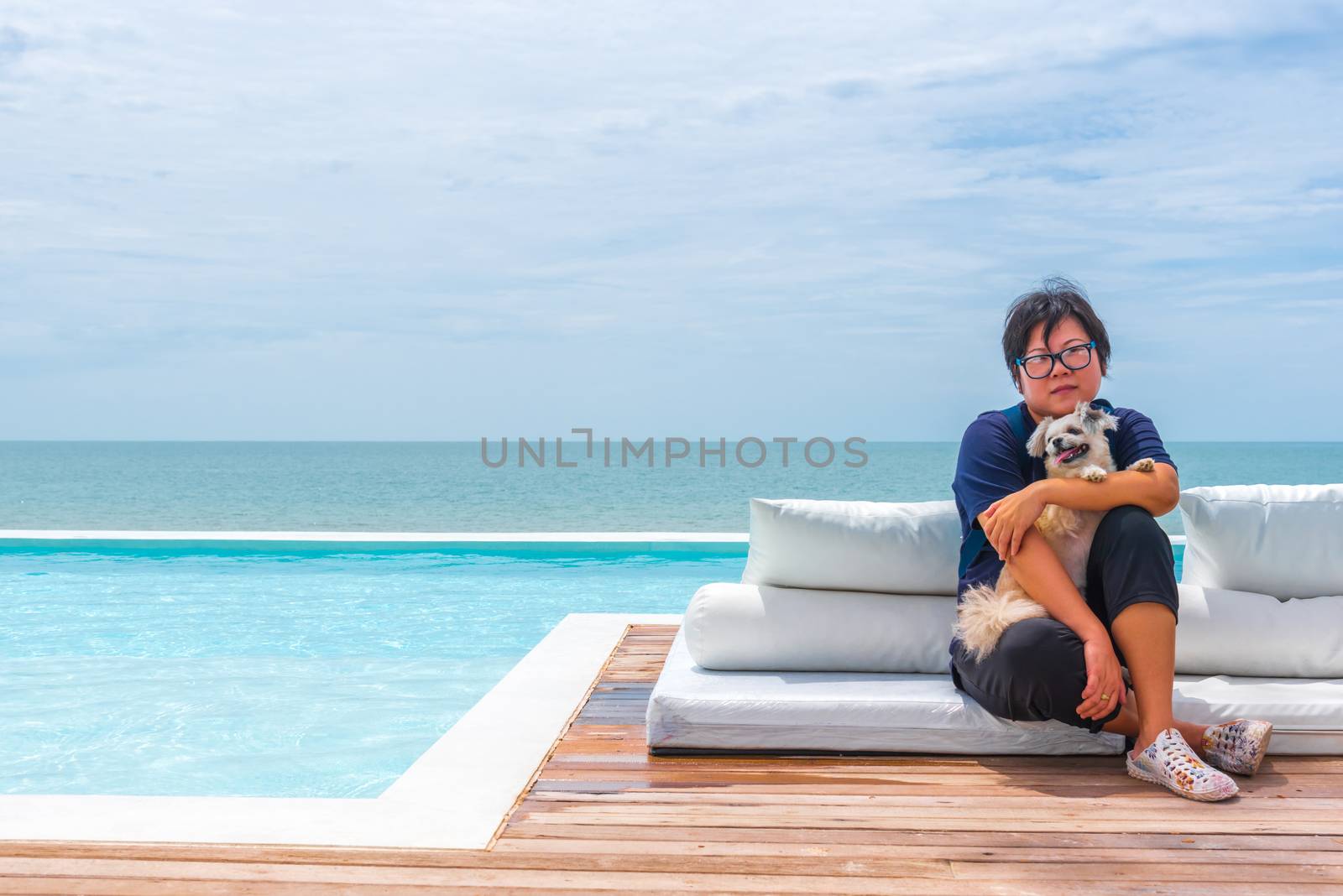 Asian woman and dog happy smile hugging on white beach bed at outdoor swimming pool seaside turquoise sea or ocean with horizon of blue sky at resort or hotel when vacation travel for relax