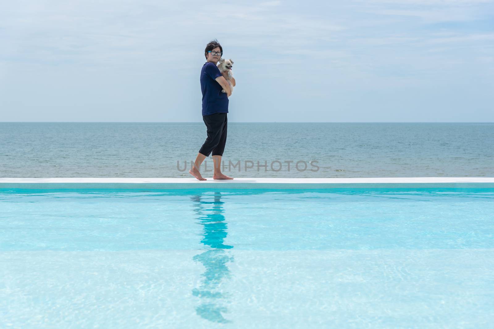 Asian woman and dog happy smile hugging at outdoor swimming pool seaside turquoise sea or ocean with horizon of blue sky at resort or hotel when vacation travel for relax