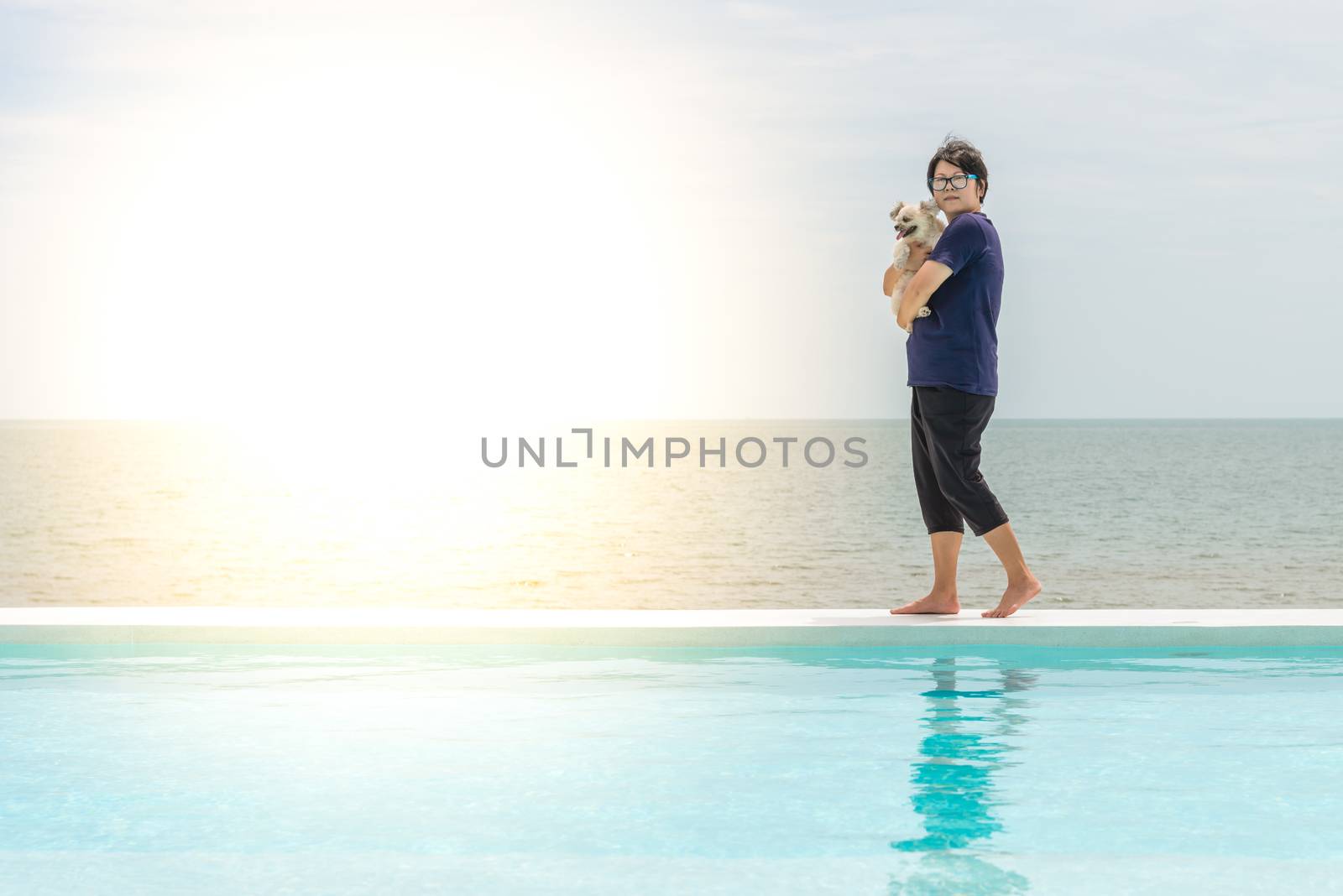 Asian woman and dog happy smile hugging at outdoor swimming pool seaside turquoise sea or ocean with horizon of blue sky at resort or hotel when vacation travel for relax