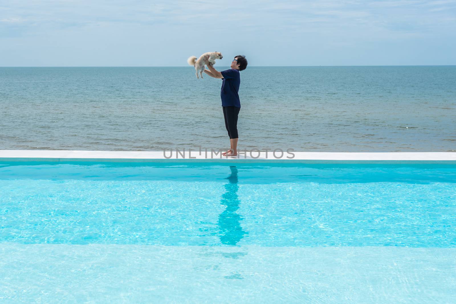 Asian woman and dog happy smile hugging at outdoor swimming pool seaside turquoise sea or ocean with horizon of blue sky at resort or hotel when vacation travel for relax