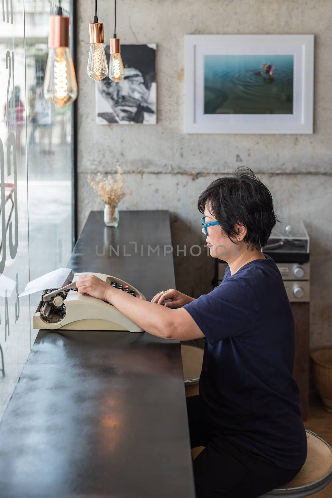 Asian woman 40s white skin with eyeglass sitting for writing something by vintage typewriter in a coffee shop cafe